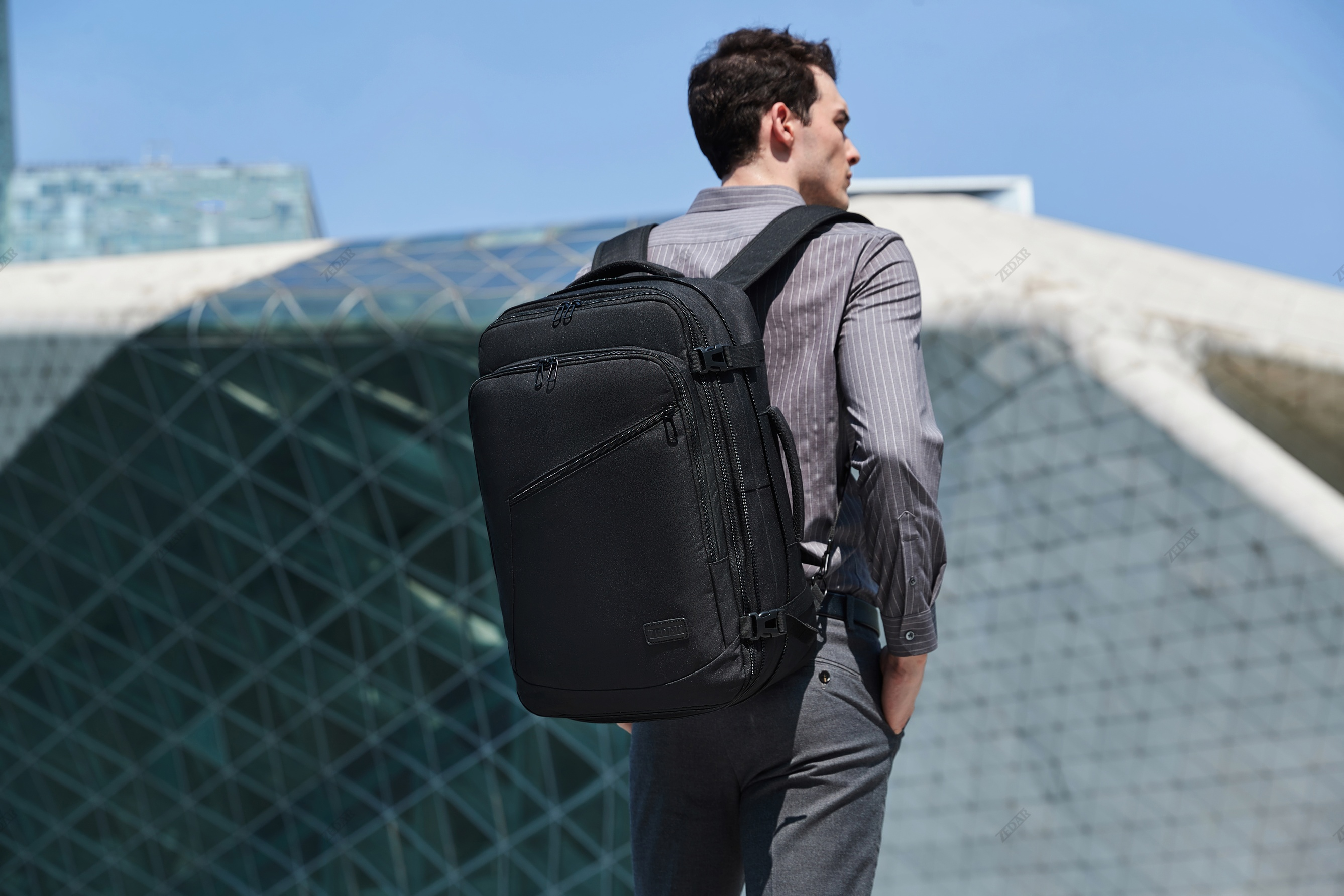 A man with a black backpack walking, with a modern building in the background.