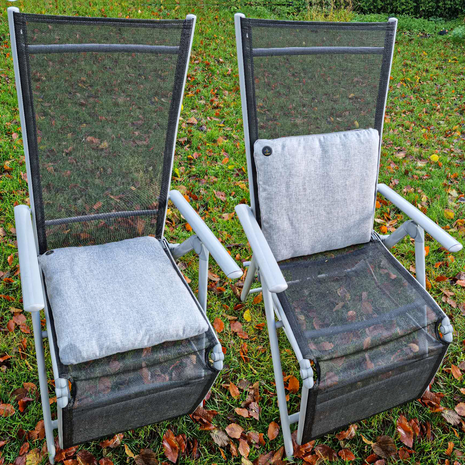 Zwei graue Gartenstühle auf Gras mit Herbstlaub.