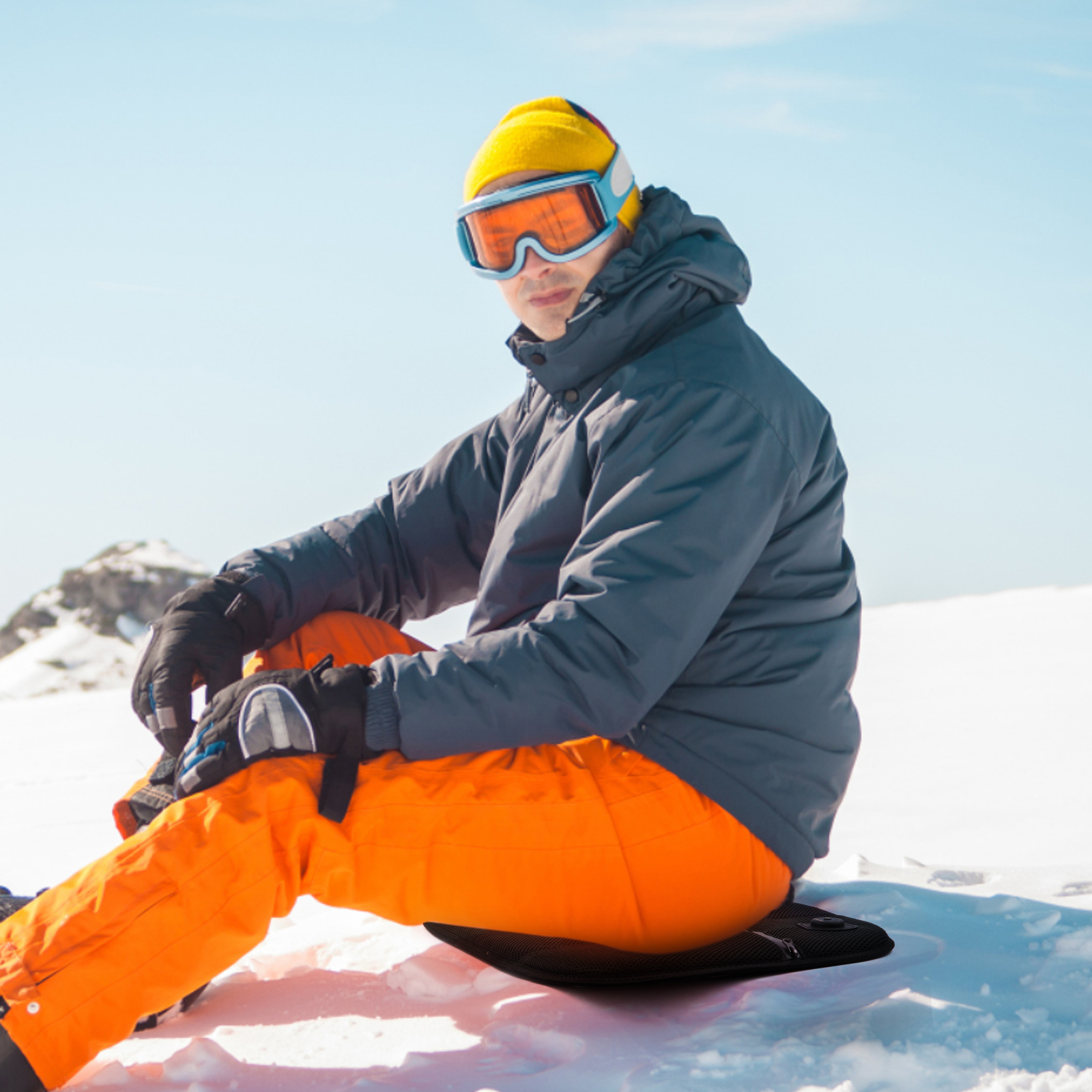 Mann in Skiausrüstung sitzt im Schnee. Er trägt einen gelben Hut und eine Skibrille.