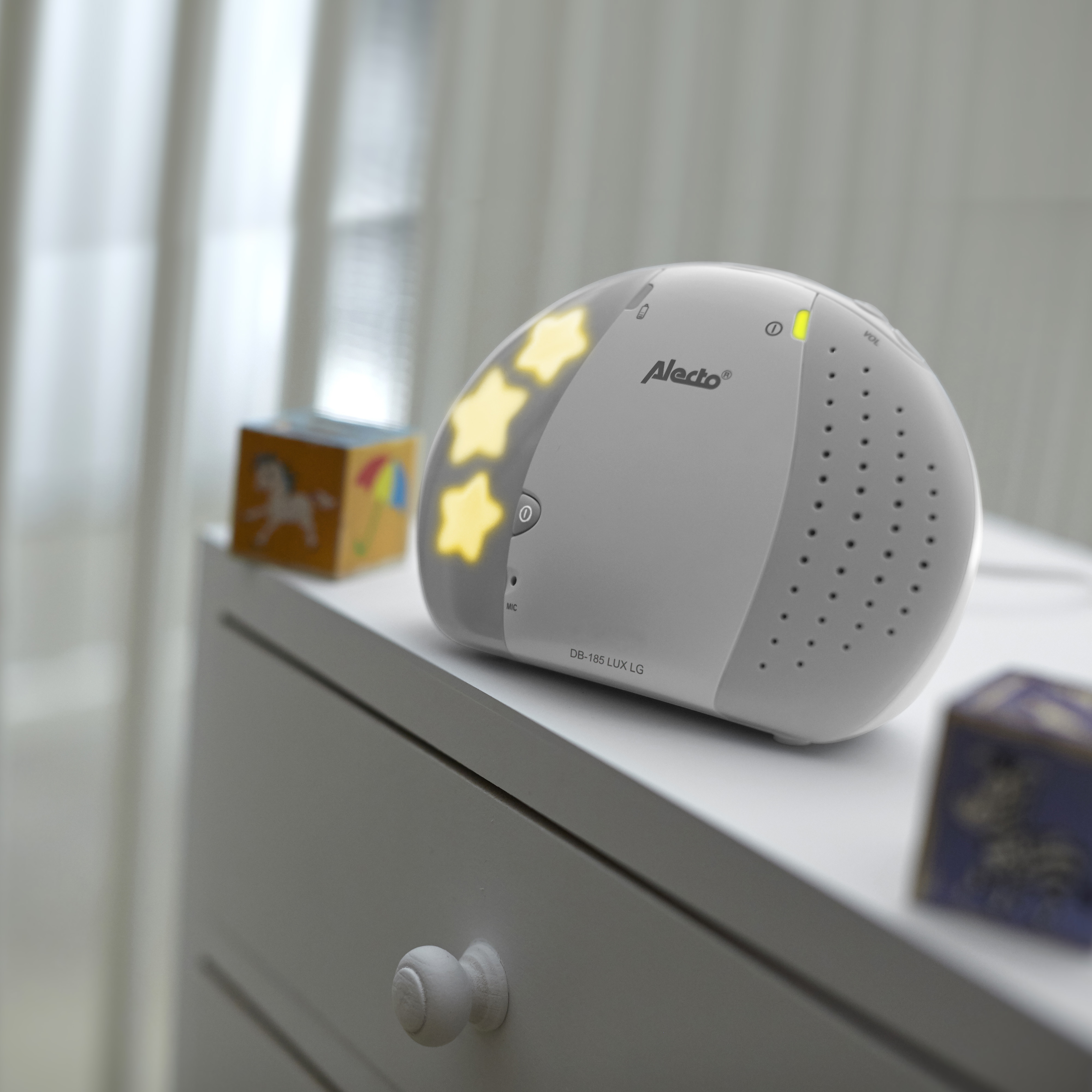 White baby monitor with stars, a toy block on a white dresser.