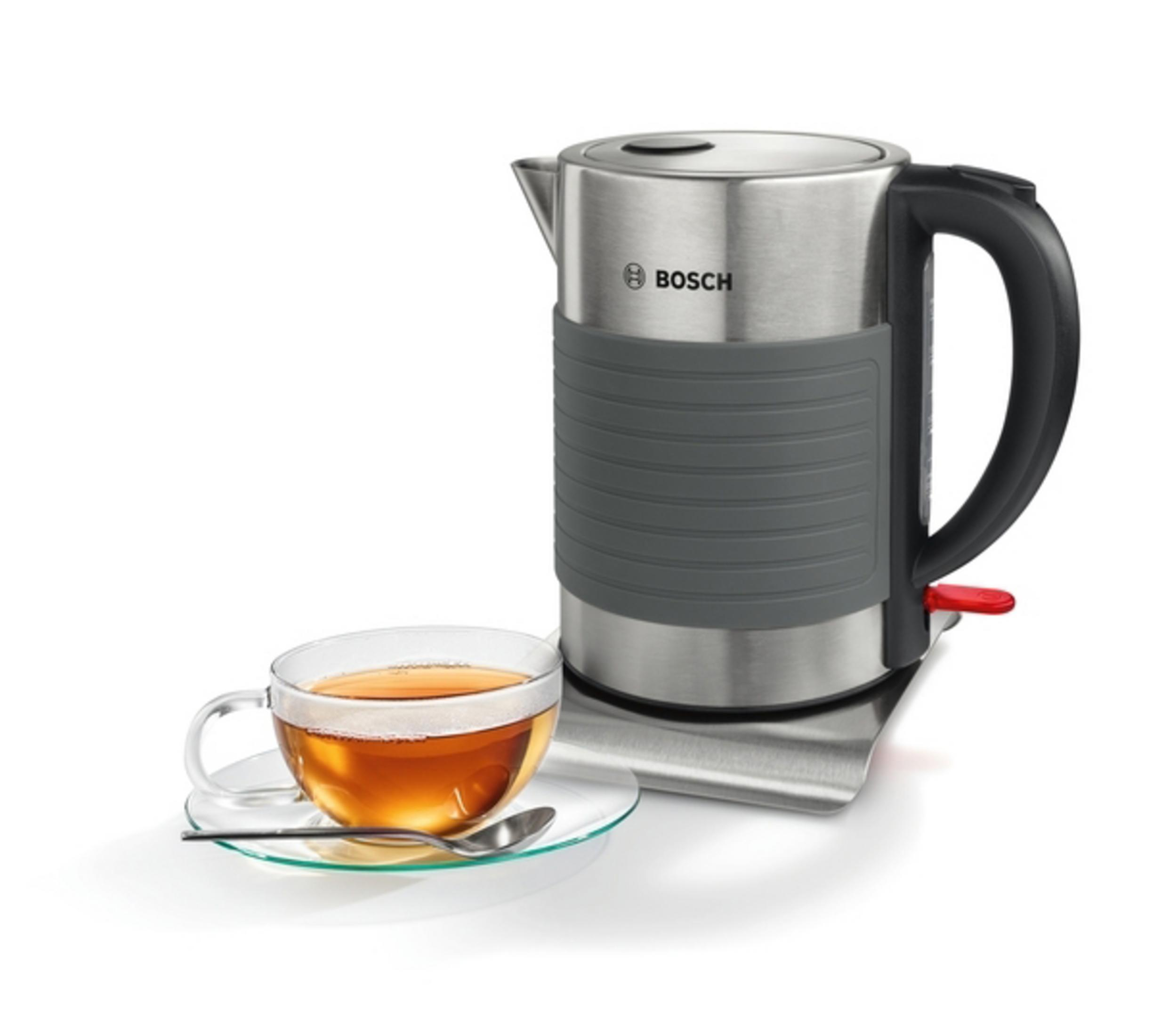 Silberner und grauer Bosch Wasserkocher mit einer Tasse Tee. Der Wasserkocher steht auf einem Metallsockel.