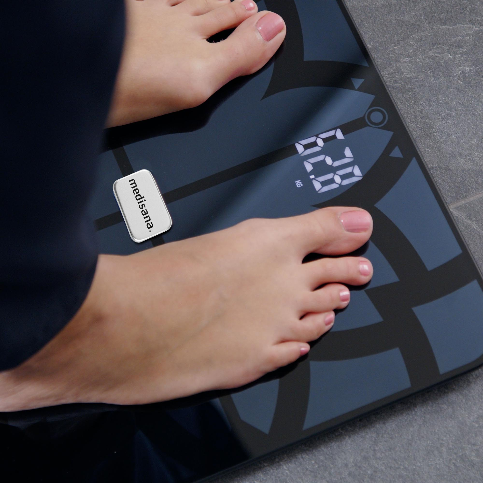 De voeten van een persoon staan op een zwarte weegschaal met 62,8 kg. Een wit 'medisana' label is zichtbaar.