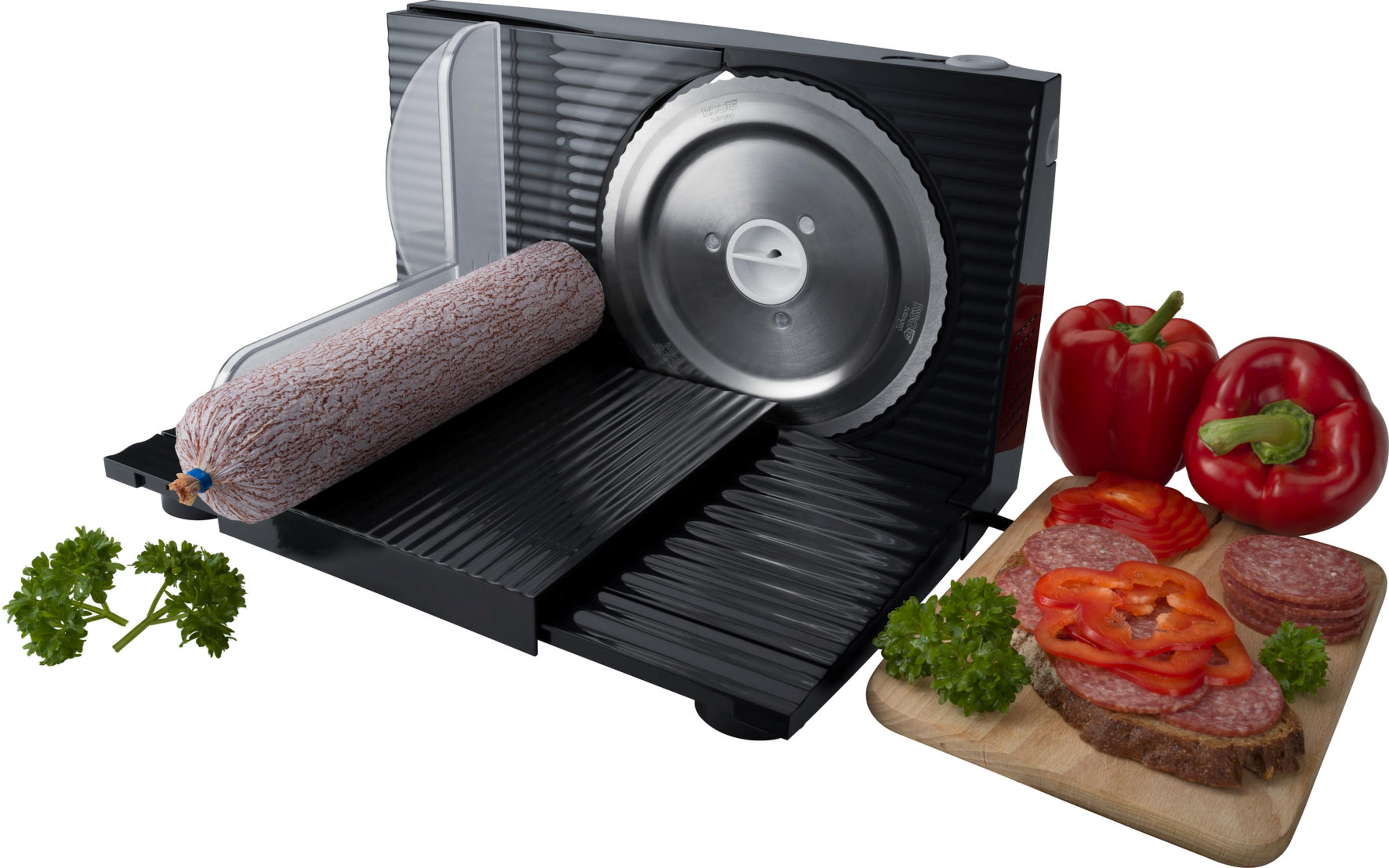 Eine schwarze Fleischschneidemaschine mit Salami und Gemüse. Geschnittene Salami auf einem Schneidebrett. Rote Paprika sind sichtbar.
