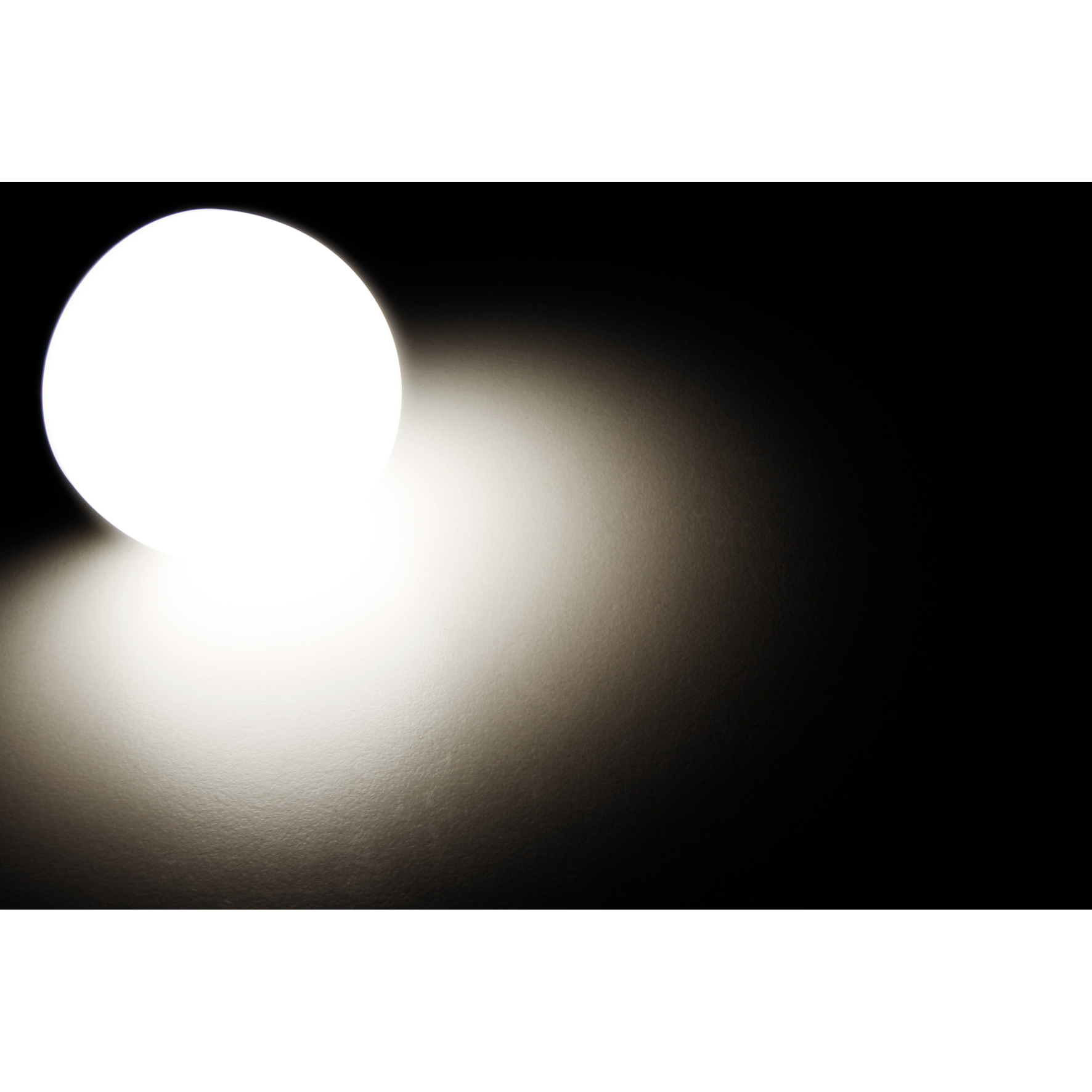 Eine helle Lichtquelle vor schwarzem Hintergrund, die ein weiches Leuchten wirft.