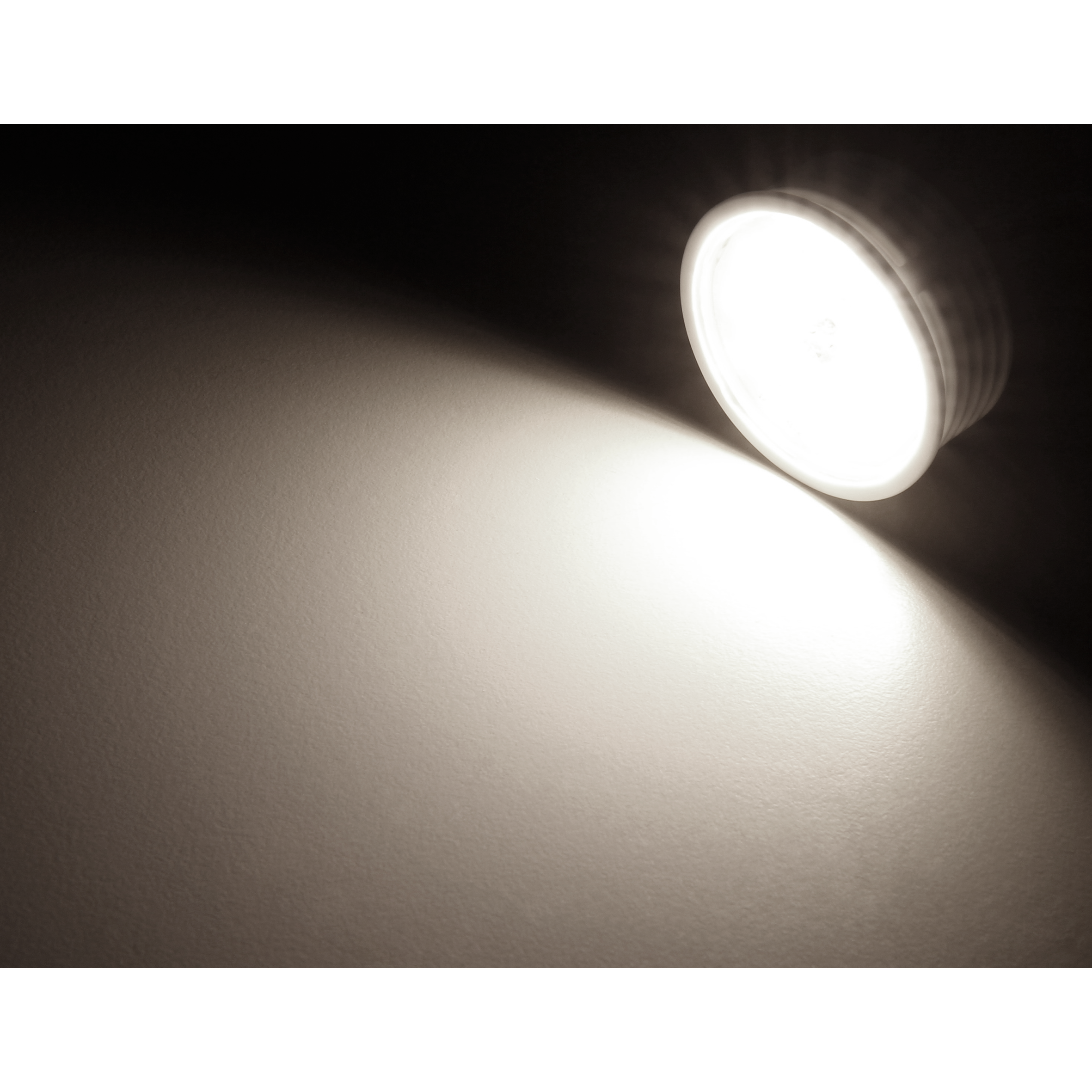 Ein heller, weißer LED-Spot scheint auf eine Wand und beleuchtet einen großen Bereich, wodurch ein Kontrast entsteht.