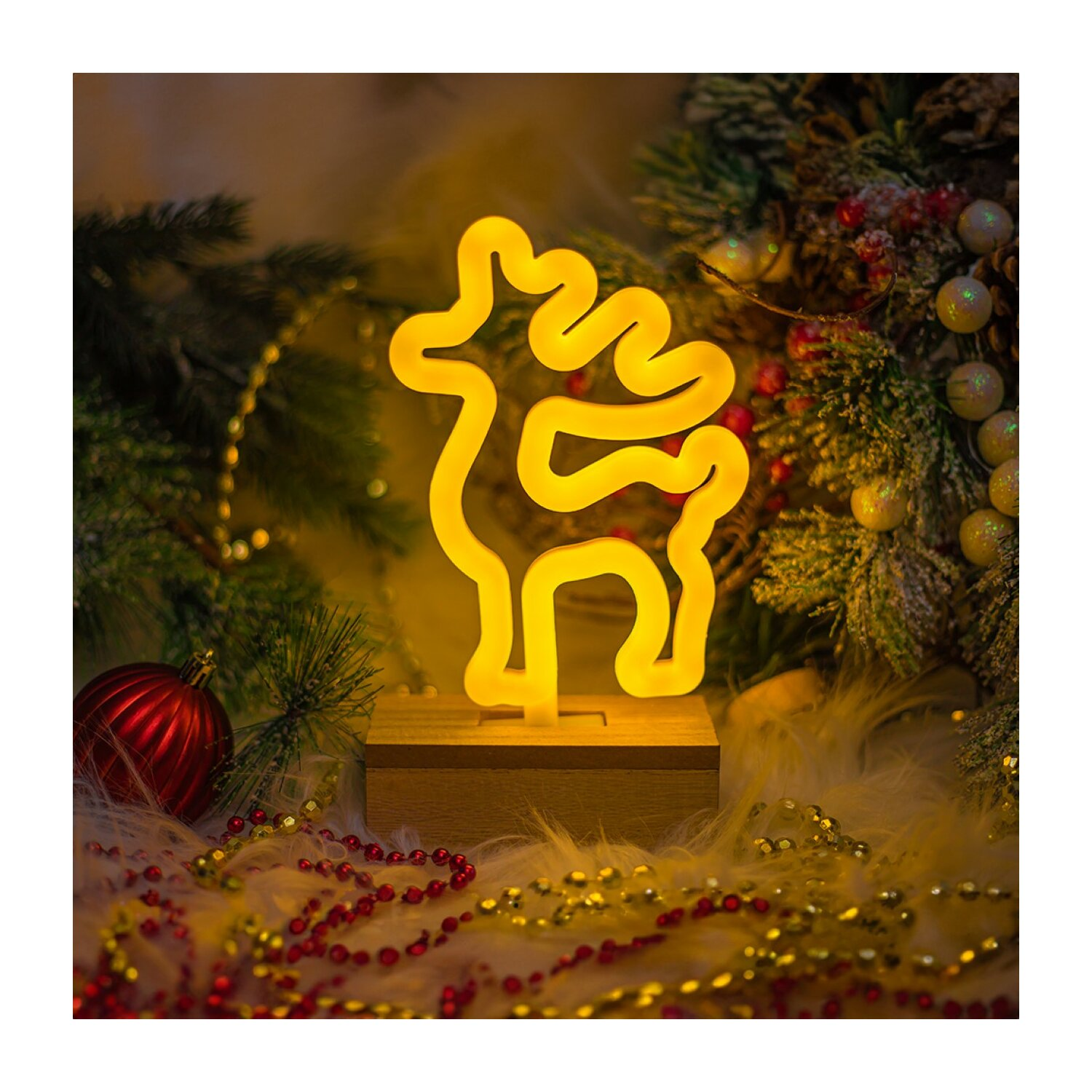 Ein neonfarbenes Rentierlicht auf Holzsockel, umgeben von Weihnachtsdekoration und dunklem Hintergrund.