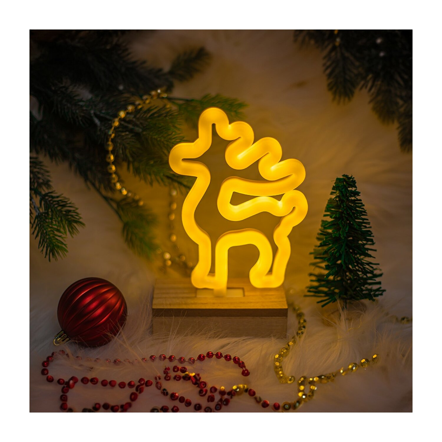 Neon-Rentier-Ornament mit Weihnachtsdekorationen. Roter Ball, Baum und goldene Schnur auf Fell.