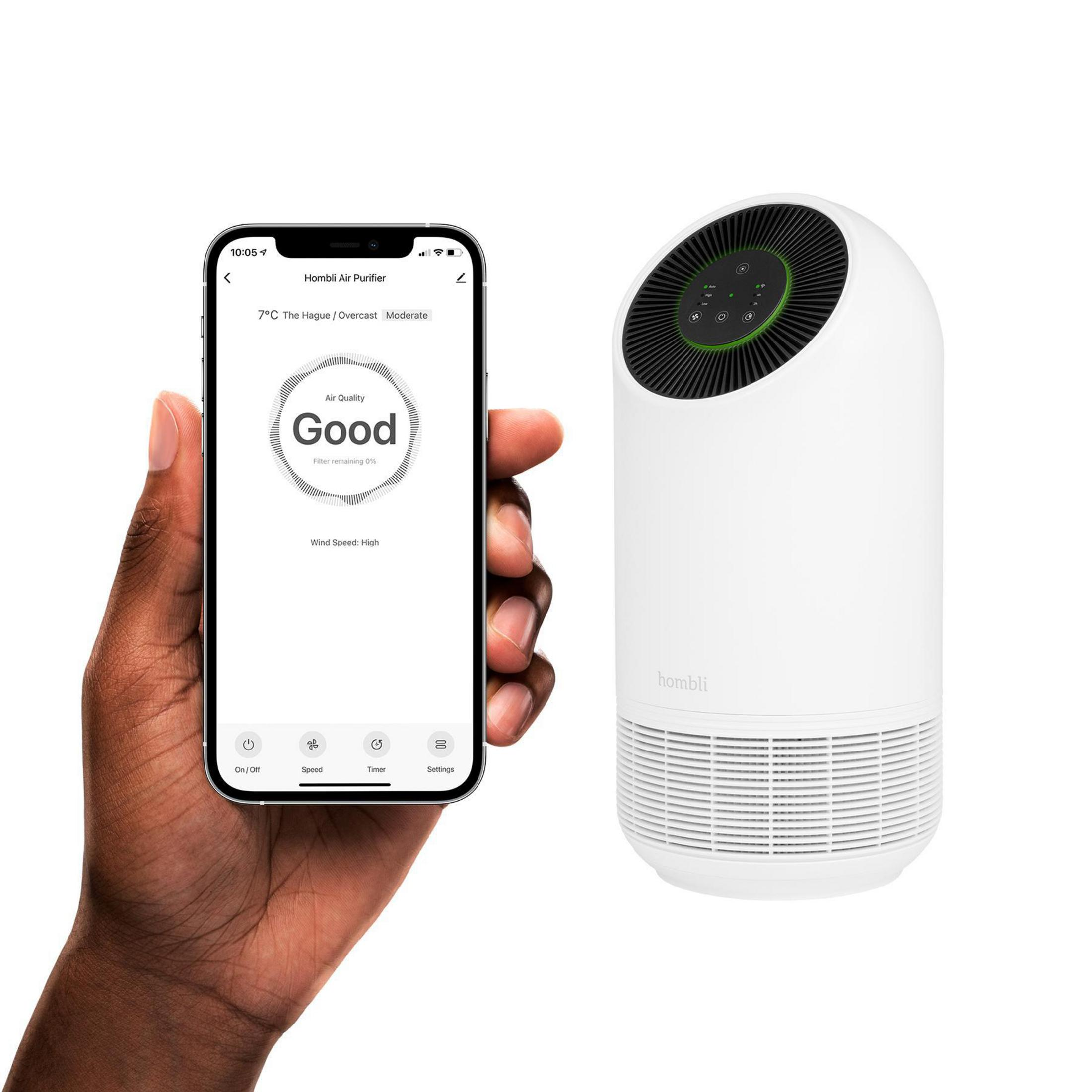 Mano che tiene un telefono che mostra la qualità dell'aria, accanto a un purificatore d'aria bianco. La qualità è buona.