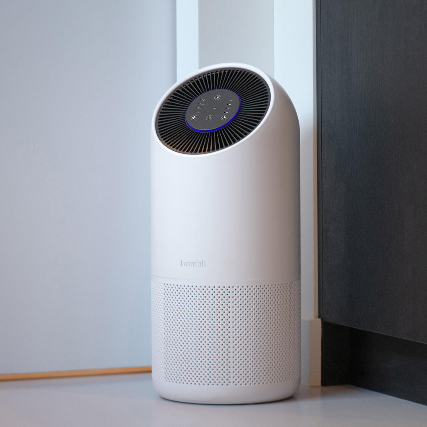 Purificatore d'aria Hombli bianco posizionato tra muro grigio e mobile scuro.