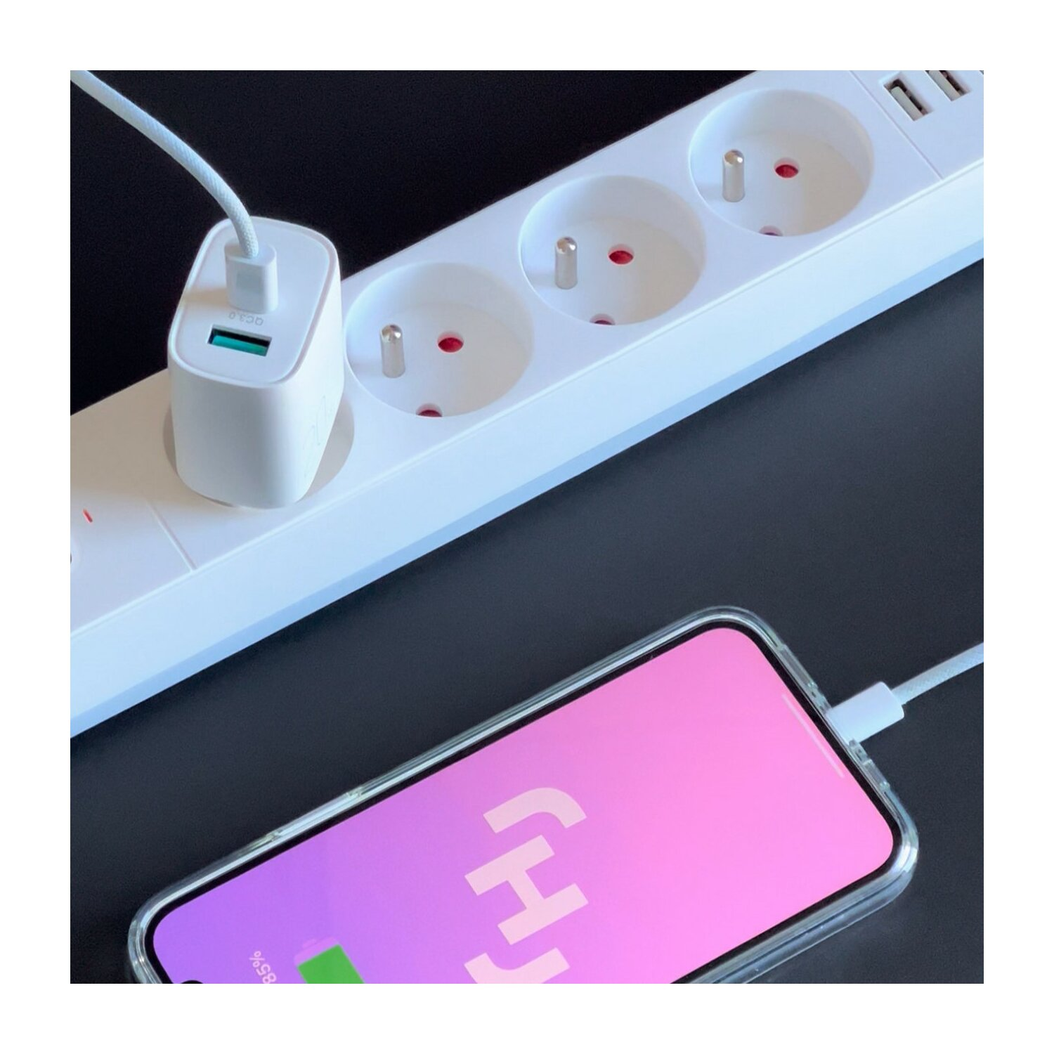 Telefon lädt mit weißem Ladegerät und Steckdosenleiste. Pinkfarbener Bildschirm zeigt Ladesymbol.