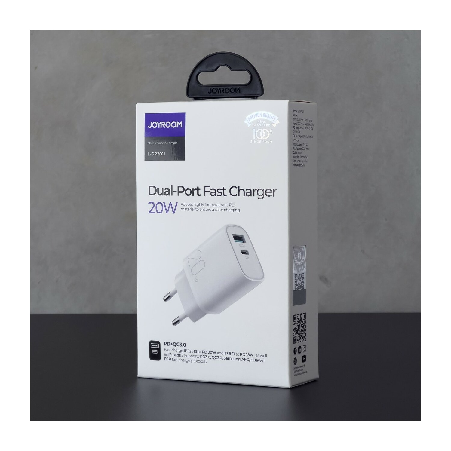 Weißes Dual-Port-Schnellladegerät mit Verpackung auf dunkler Oberfläche.