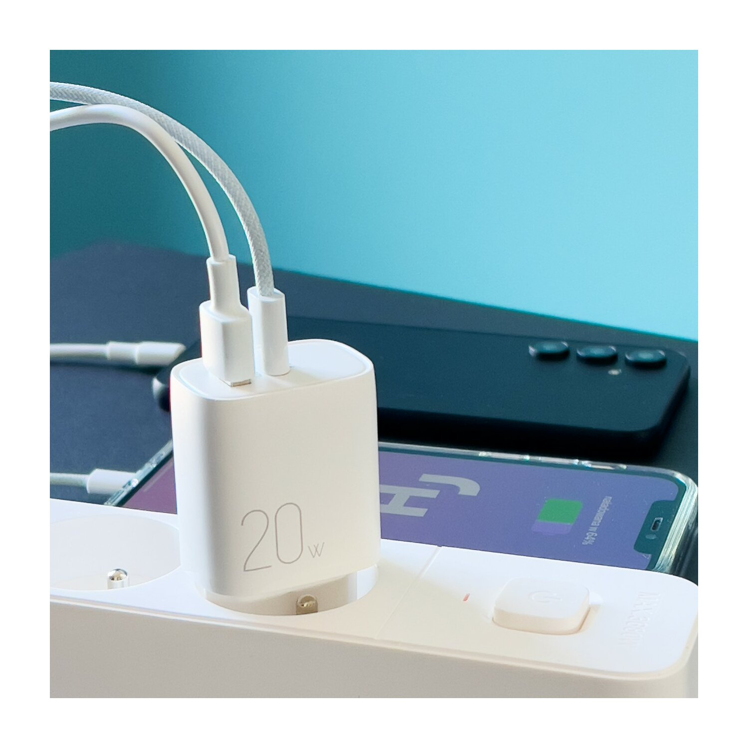 Weißes 20W Ladegerät mit zwei Kabeln, die an eine Steckdosenleiste angeschlossen sind, daneben ein ladendes Telefon.
