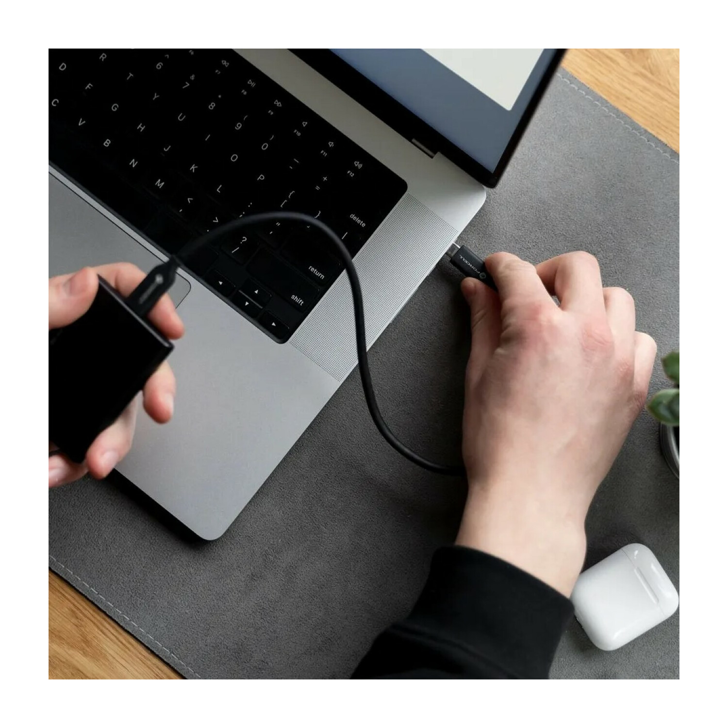 Hände, die ein schwarzes USB-C-Kabel mit einem Laptop und einer schwarzen externen Festplatte verbinden.