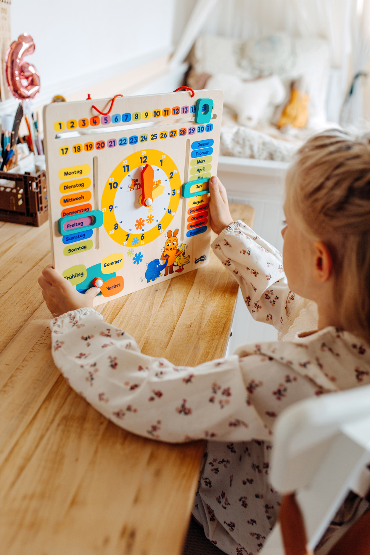 Una bambina tiene in mano un orologio calendario di legno. L'orologio mostra ora, data e giorno.
