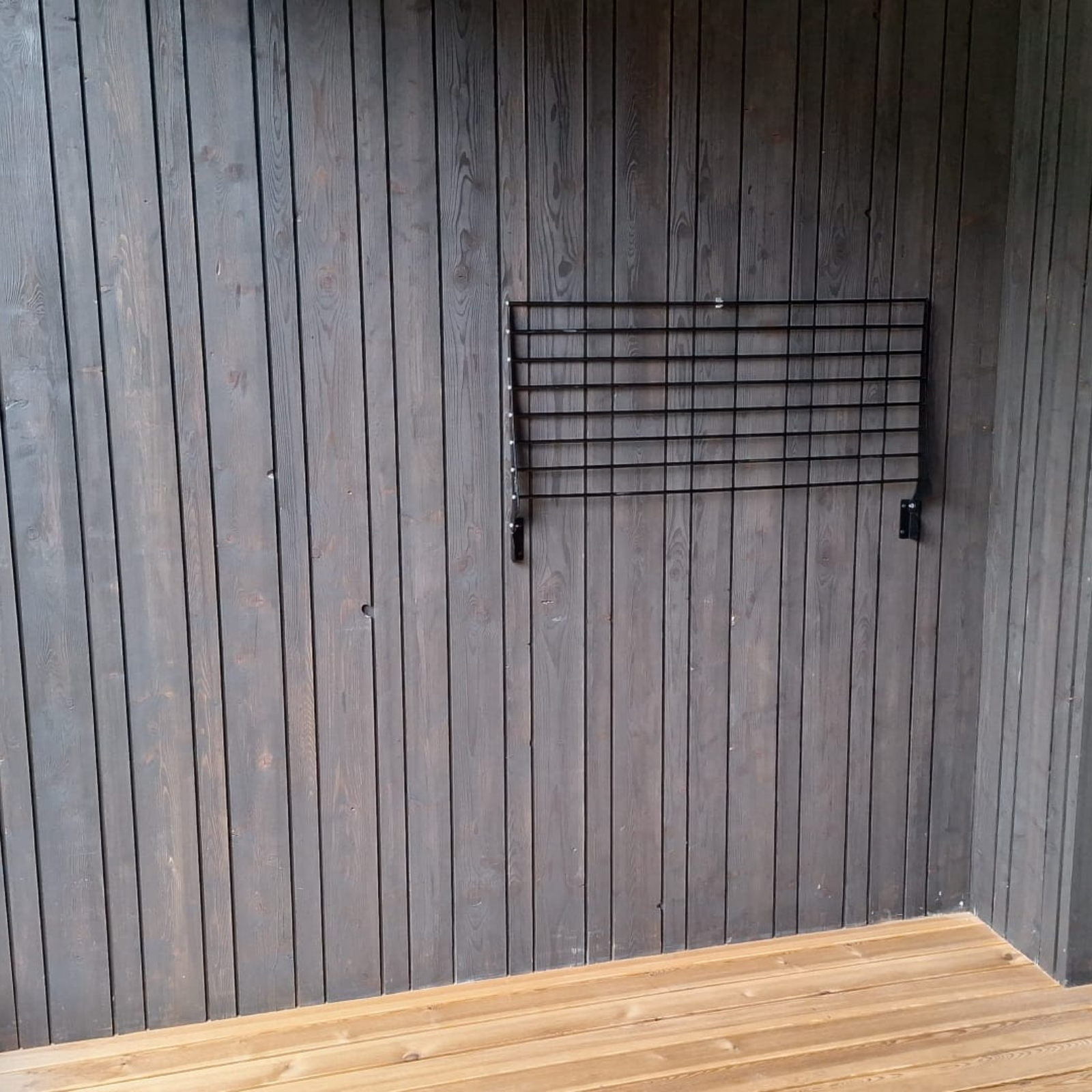 Muro in legno con griglia metallica nera attaccata. Tavole di legno in primo piano.