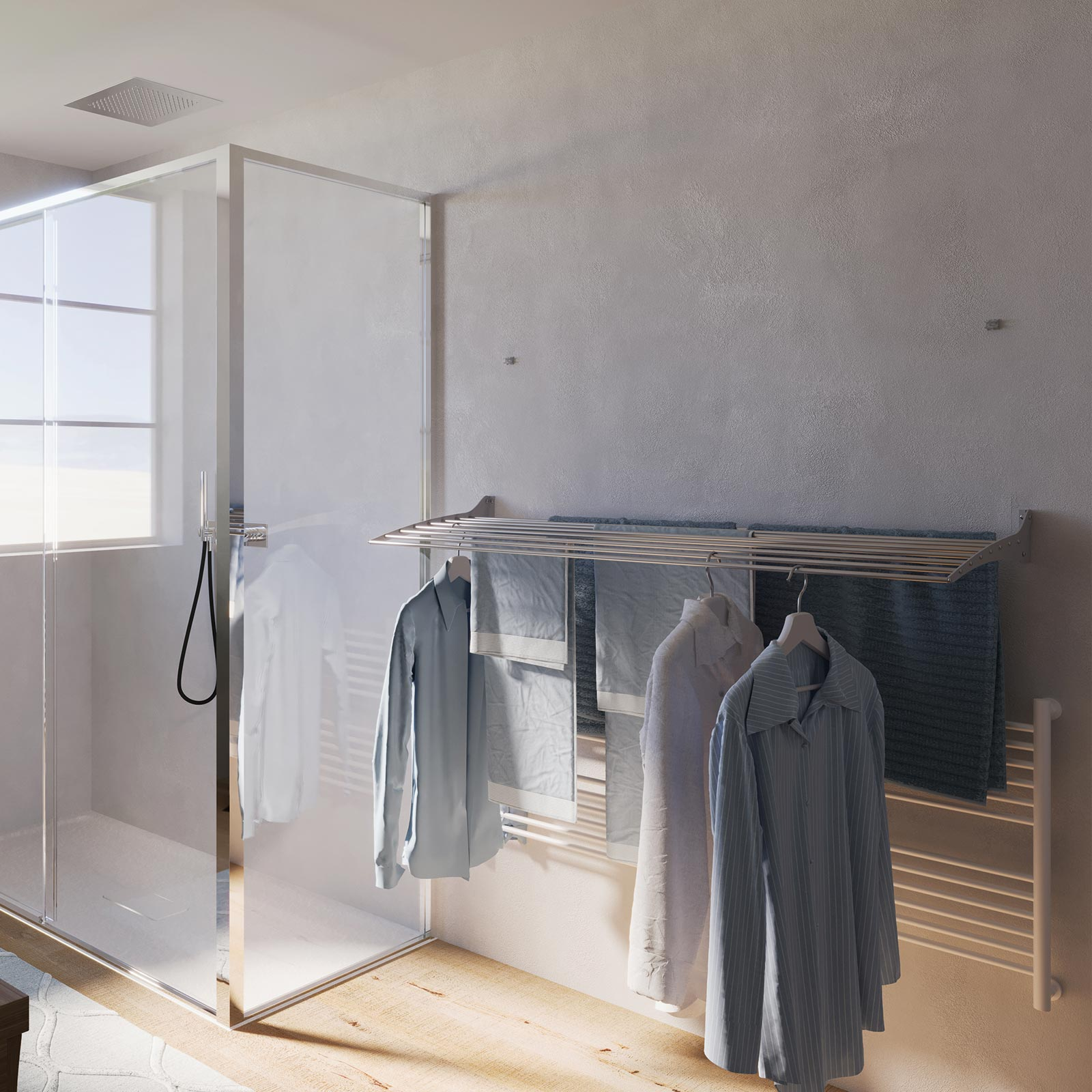 Un bagno con doccia in vetro e vestiti appesi a un portabiancheria. Camicie e asciugamani sono in mostra. Muro bianco.