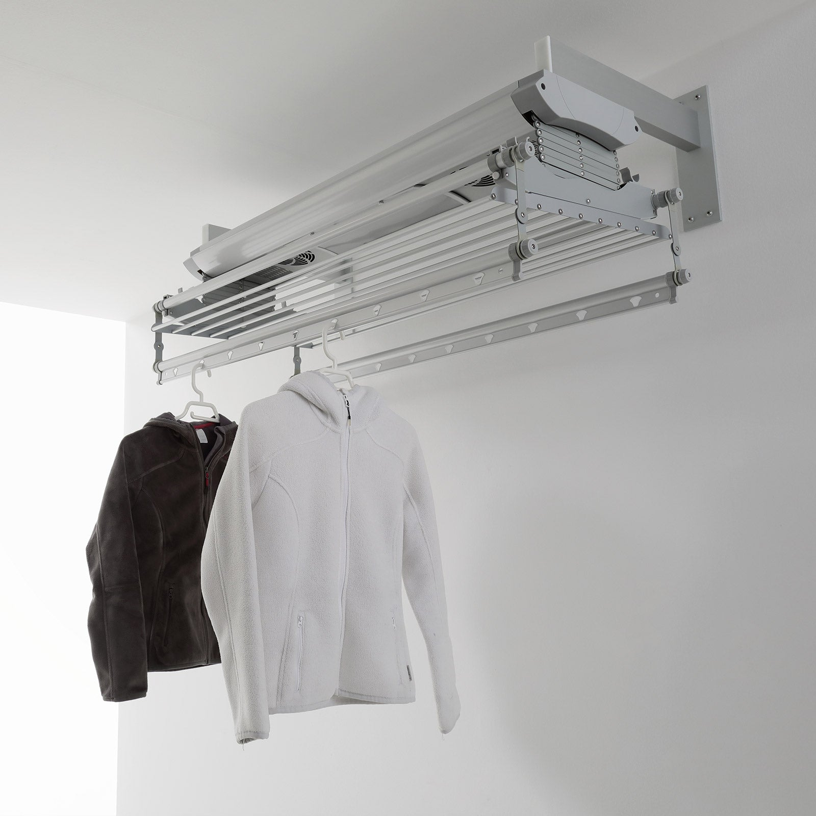 Stendibiancheria a soffitto con vestiti appesi; sfondo parete bianca.
