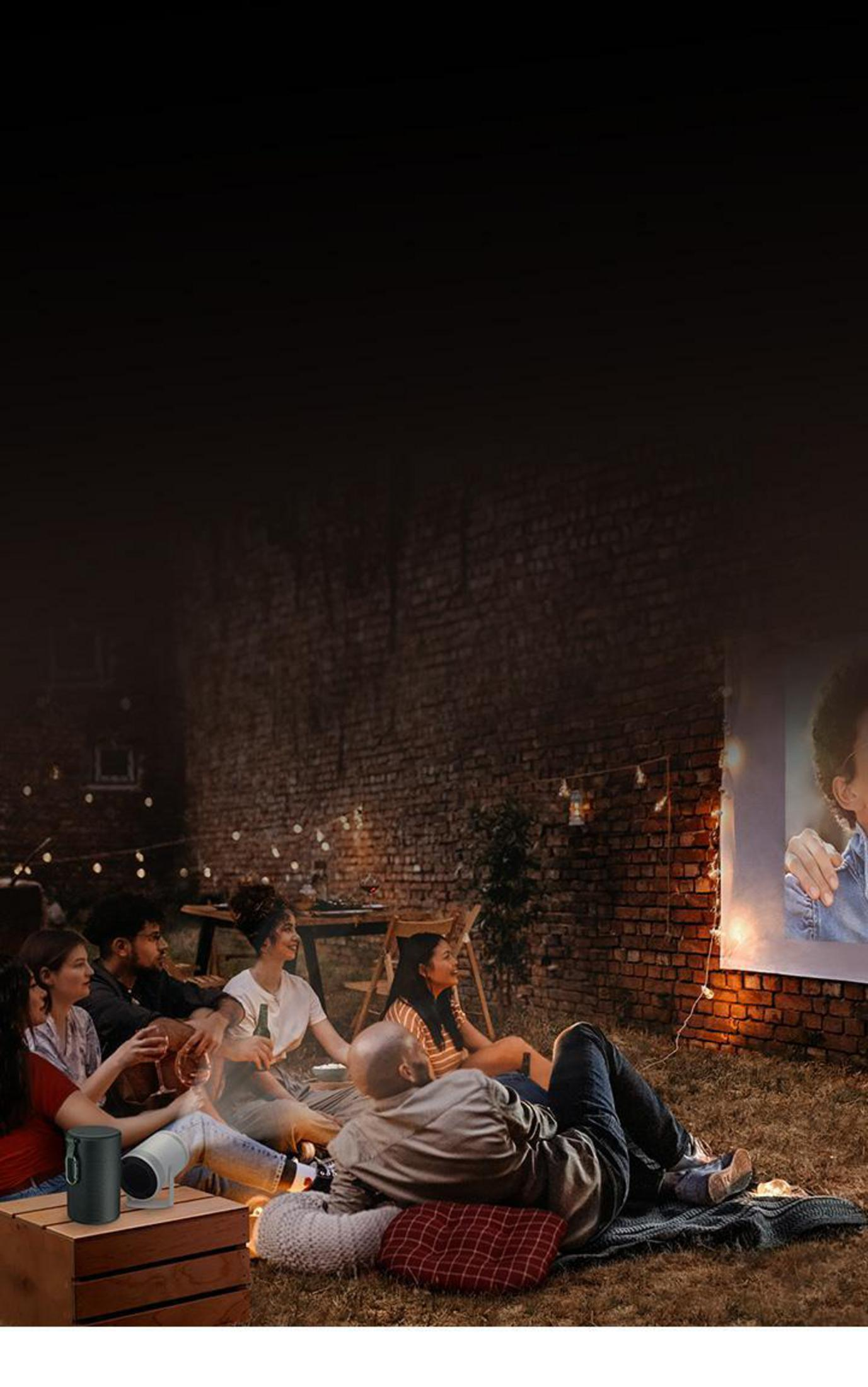 Grupo de personas viendo una película proyectada en una pared. Luz y altavoz visibles.