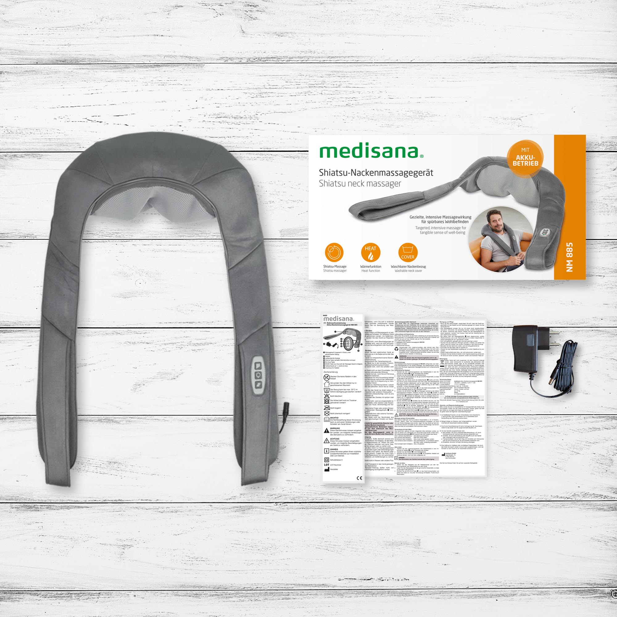 Massaggiatore per il collo shiatsu grigio, scatola e accessori su superficie di legno bianco.