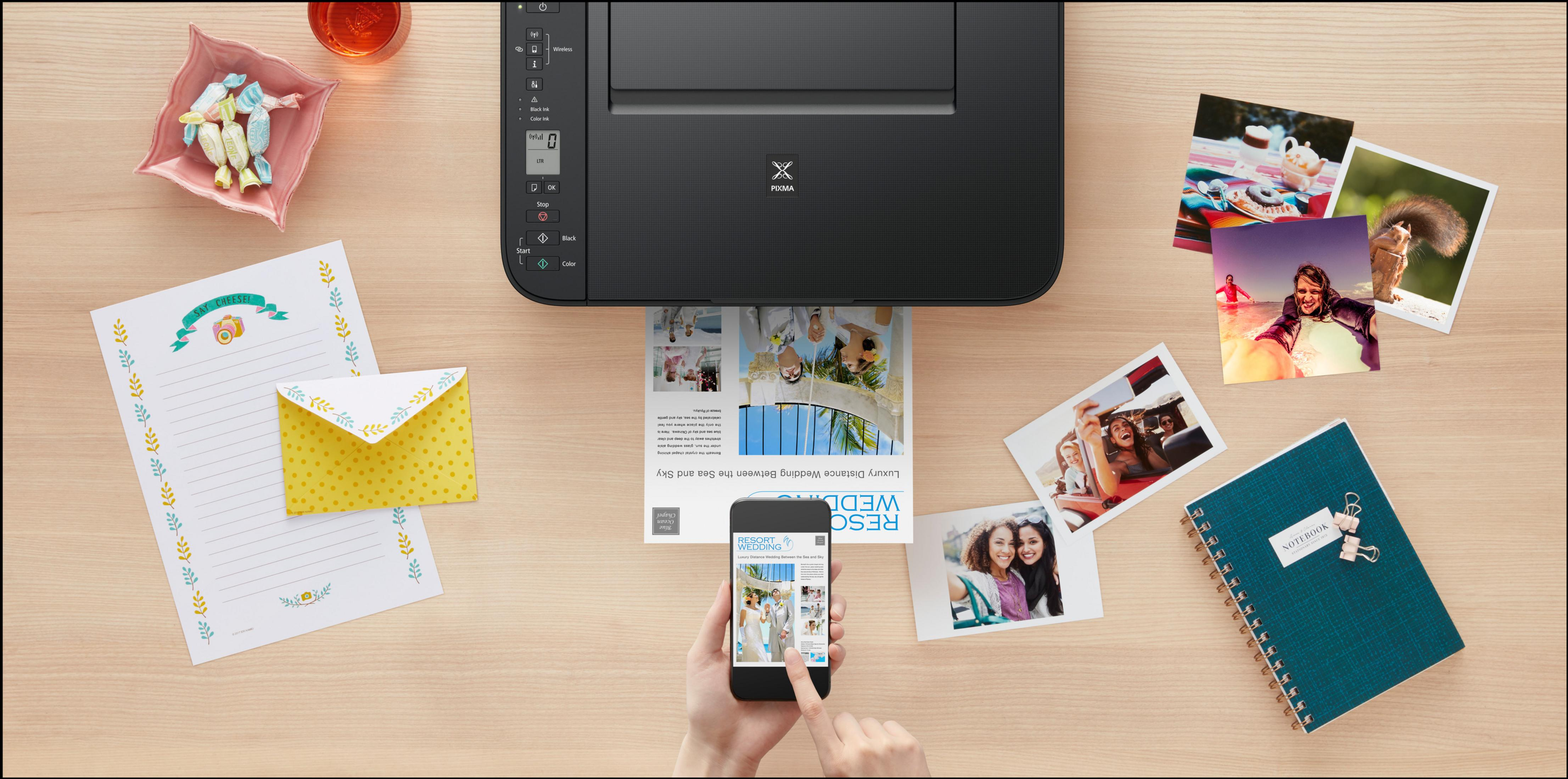 Drukarka drukuje zdjęcia. Telefon wyświetla stronę internetową, otoczoną zdjęciami i papierami.