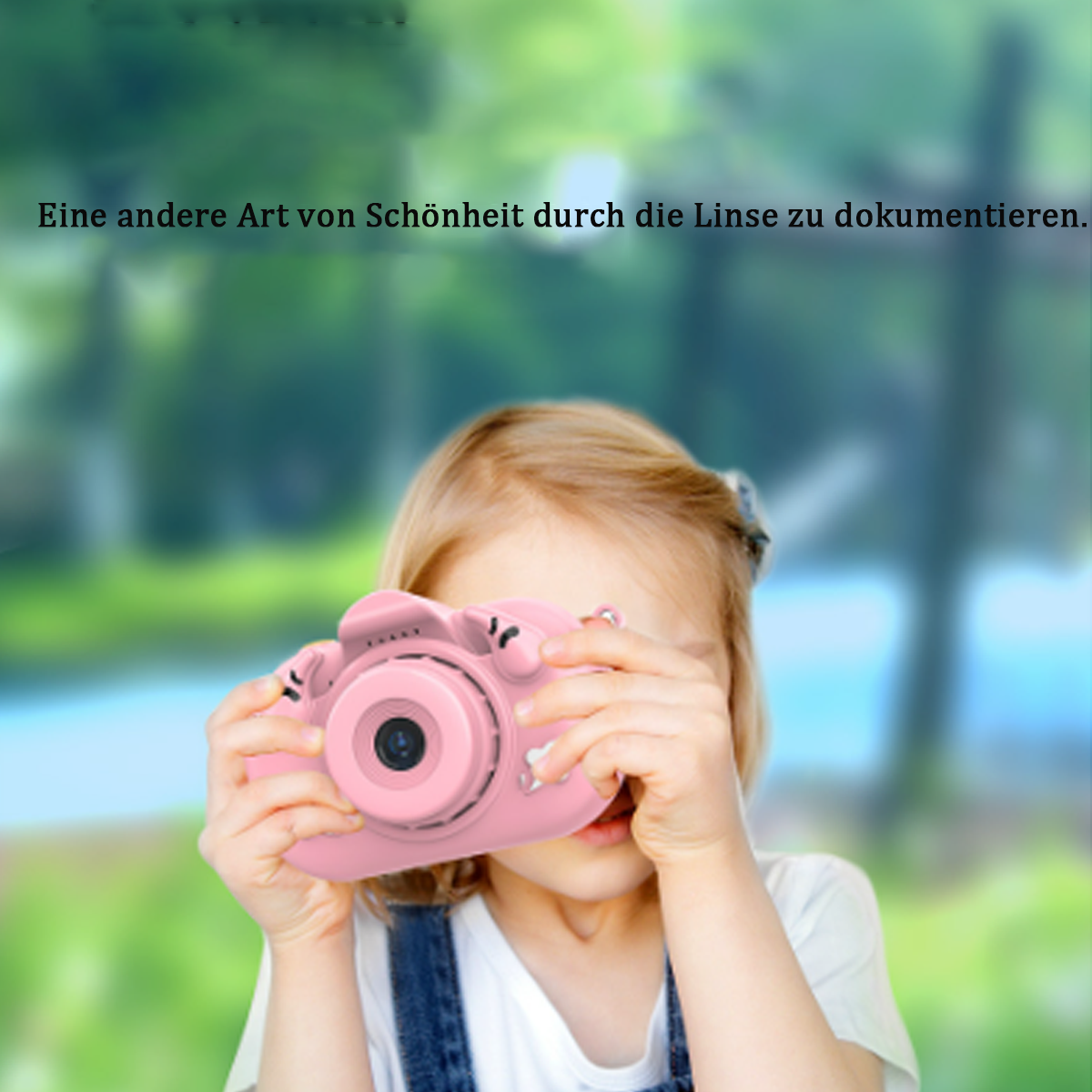 Una bambina che tiene una fotocamera rosa, guardando attraverso l'obiettivo. Sfondo verde sfocato.
