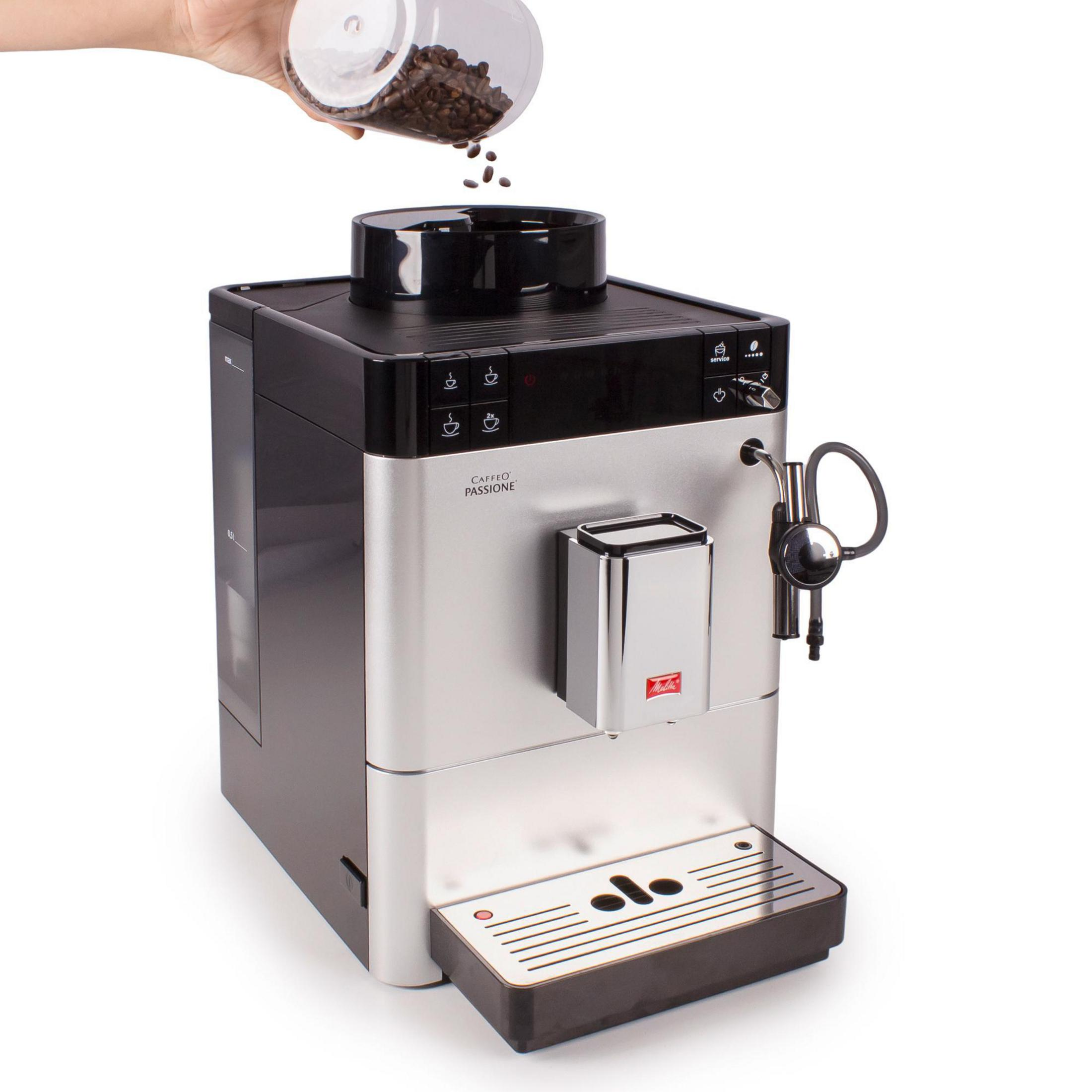 Une machine à café automatique. Une main verse des grains de café dans le haut de la machine.