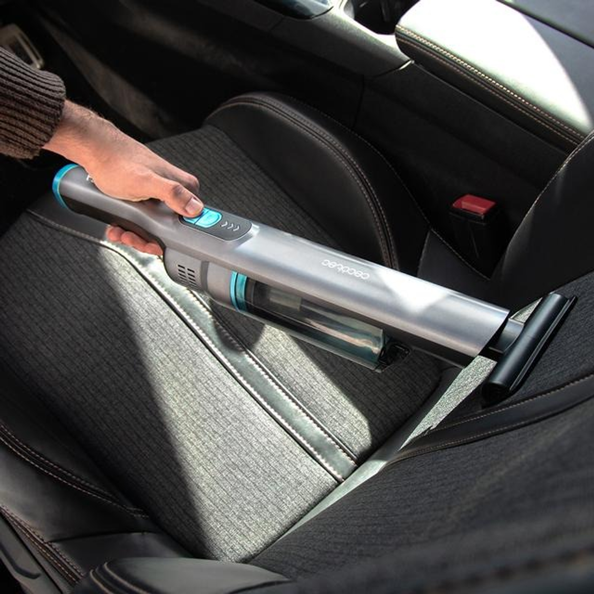 Persona che utilizza un aspirapolvere senza fili Cecotec in un'auto. Interni grigio e nero.