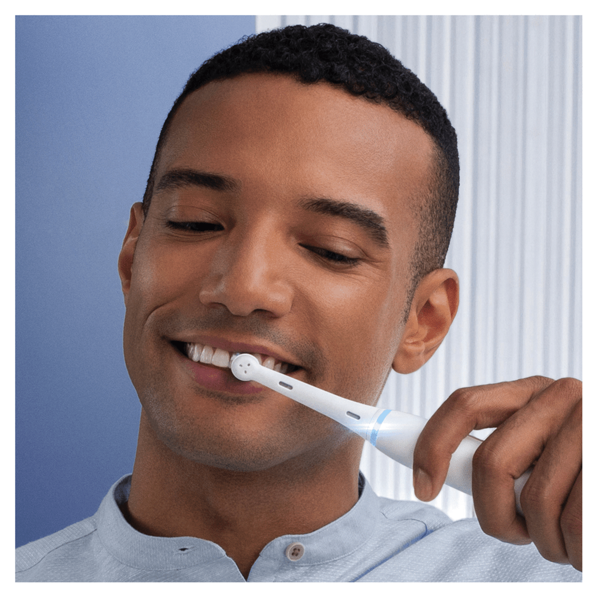 Un hombre se cepilla los dientes con un cepillo eléctrico, sonriendo. Fondo azul.