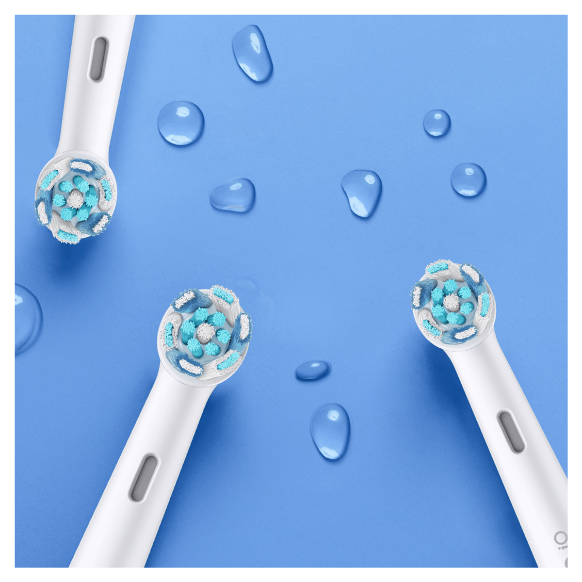 Tres cabezales de cepillo de dientes blancos con cerdas azules y blancas, gotas de agua sobre fondo azul.