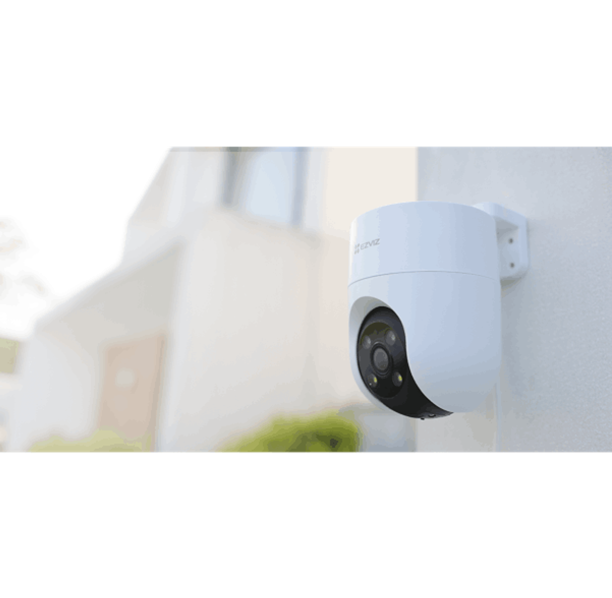 Cámara de seguridad blanca montada en una pared blanca, con una casa al fondo.