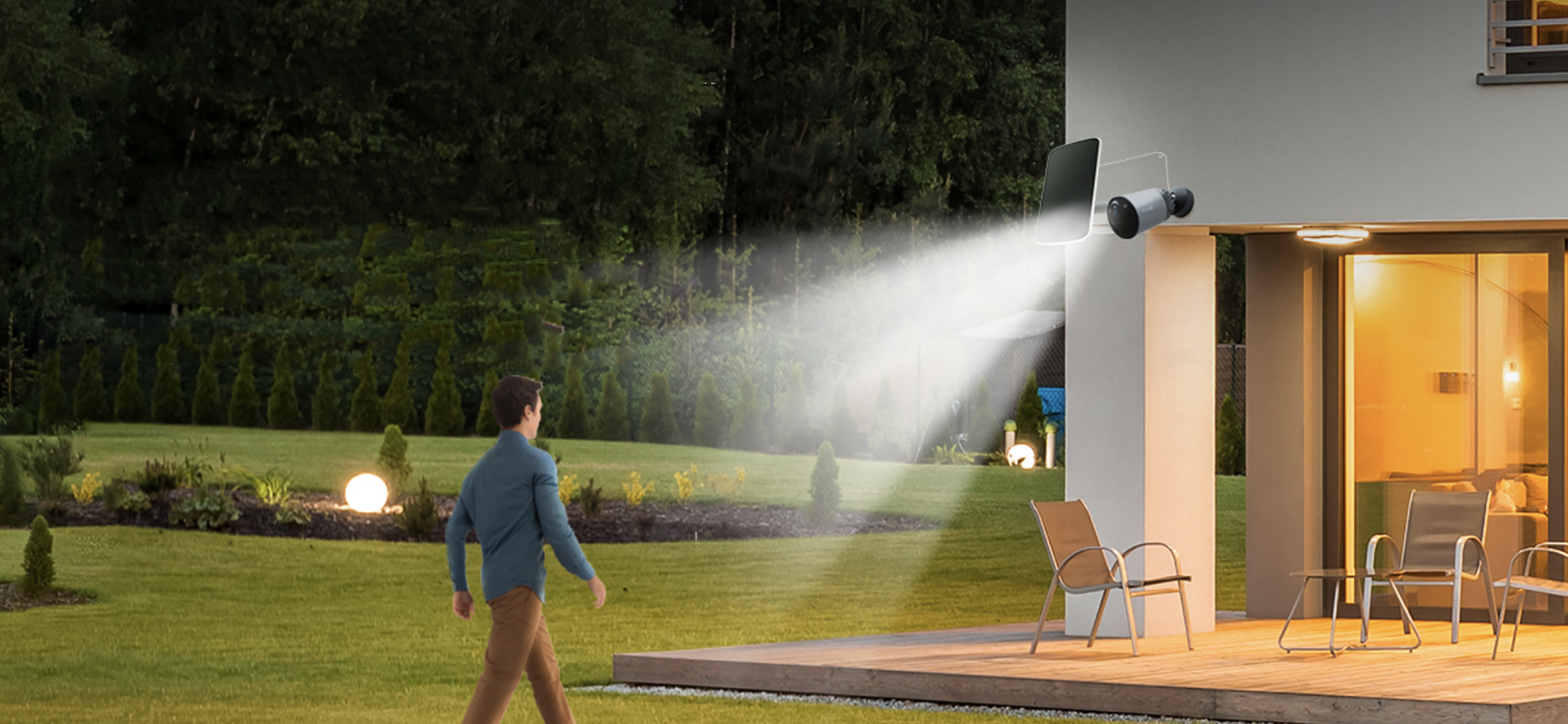 Mężczyzna idzie po patio. Światła świecą z domu i lamp bezpieczeństwa.