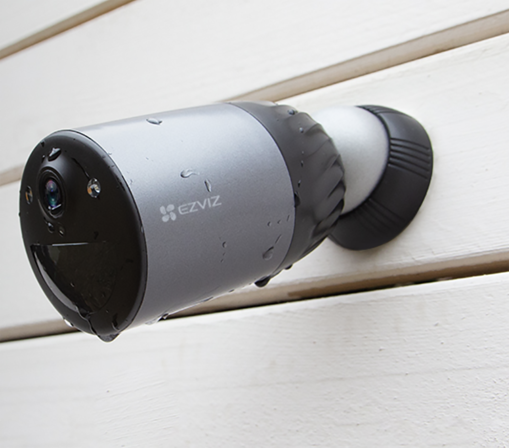 Srebrno-czarna kamera bezpieczeństwa zamontowana na białej drewnianej ścianie, widoczne logo Ezviz.