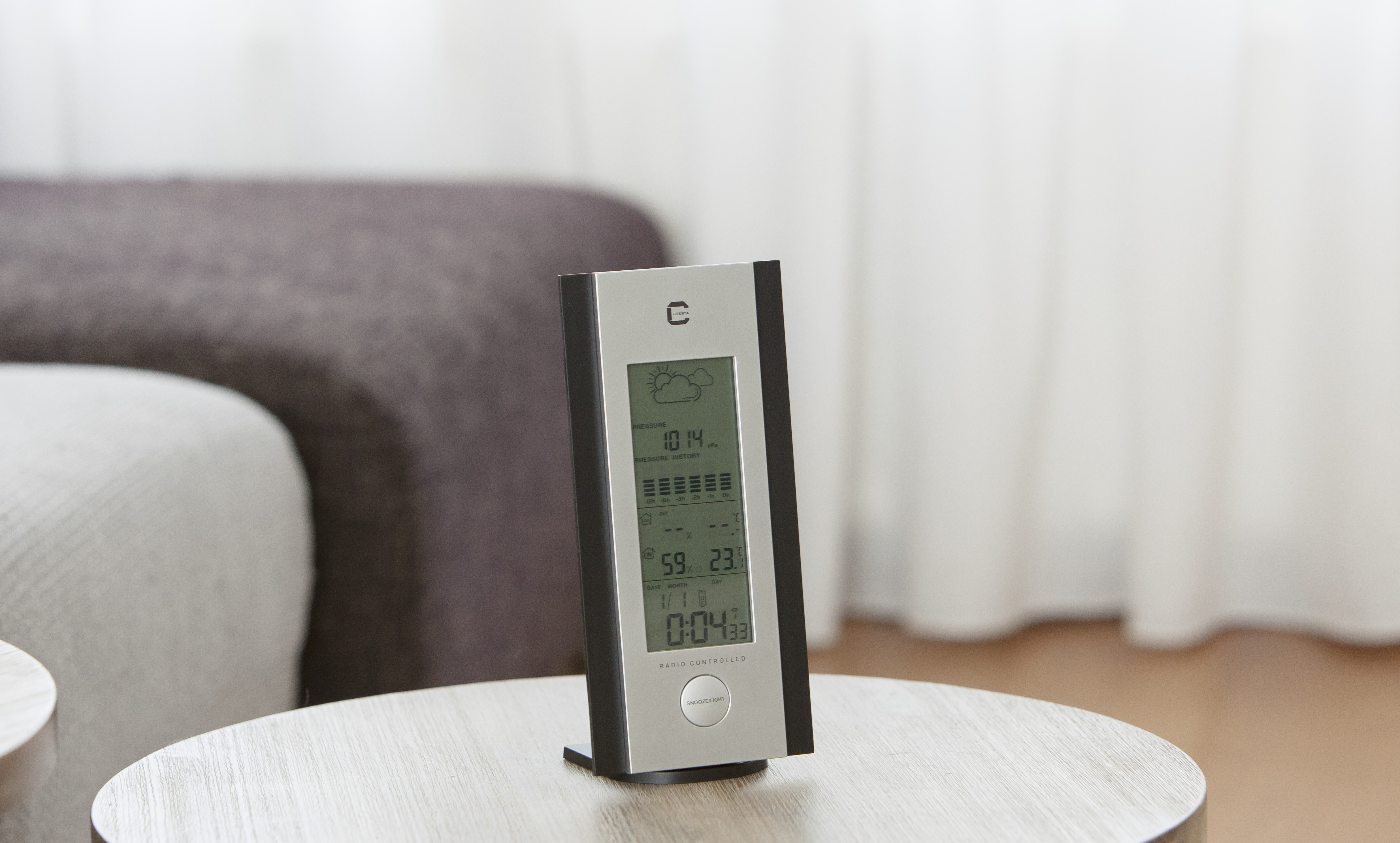 A digital weather station on a table, displaying time, weather info, and a neutral background.