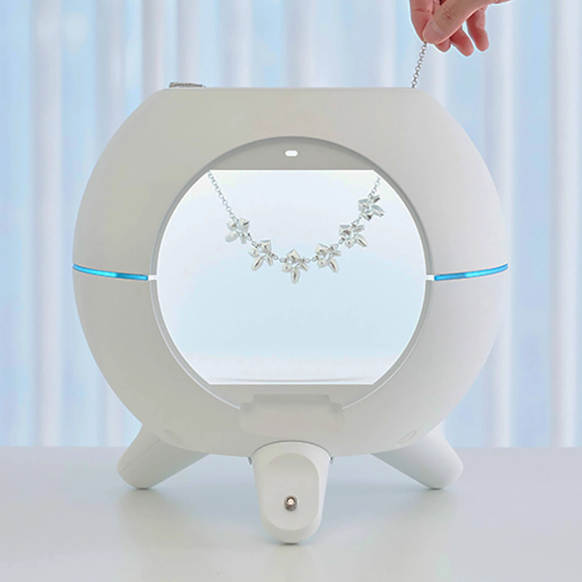 Weißes, kugelförmiges Schmuckdisplay mit Halskette und Hand.