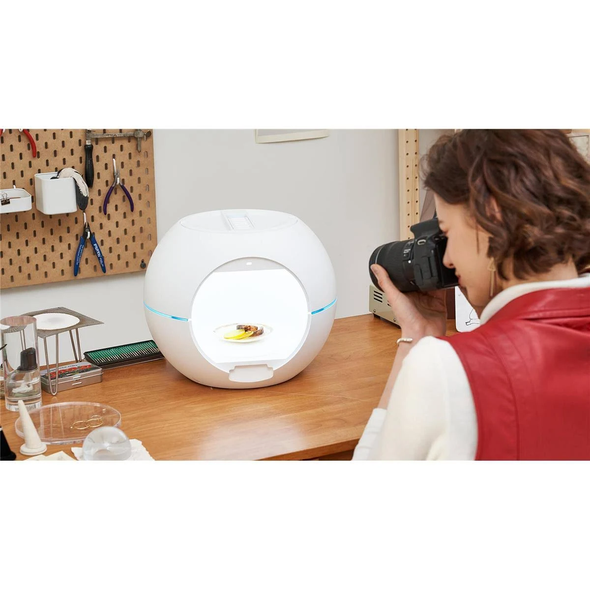 Eine Frau fotografiert Essen in einer weißen, kugelförmigen Produktfotografiebox.