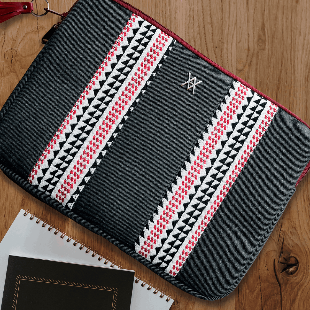 Funda de portátil de mezclilla oscura con patrón geométrico rojo, blanco y negro sobre madera.