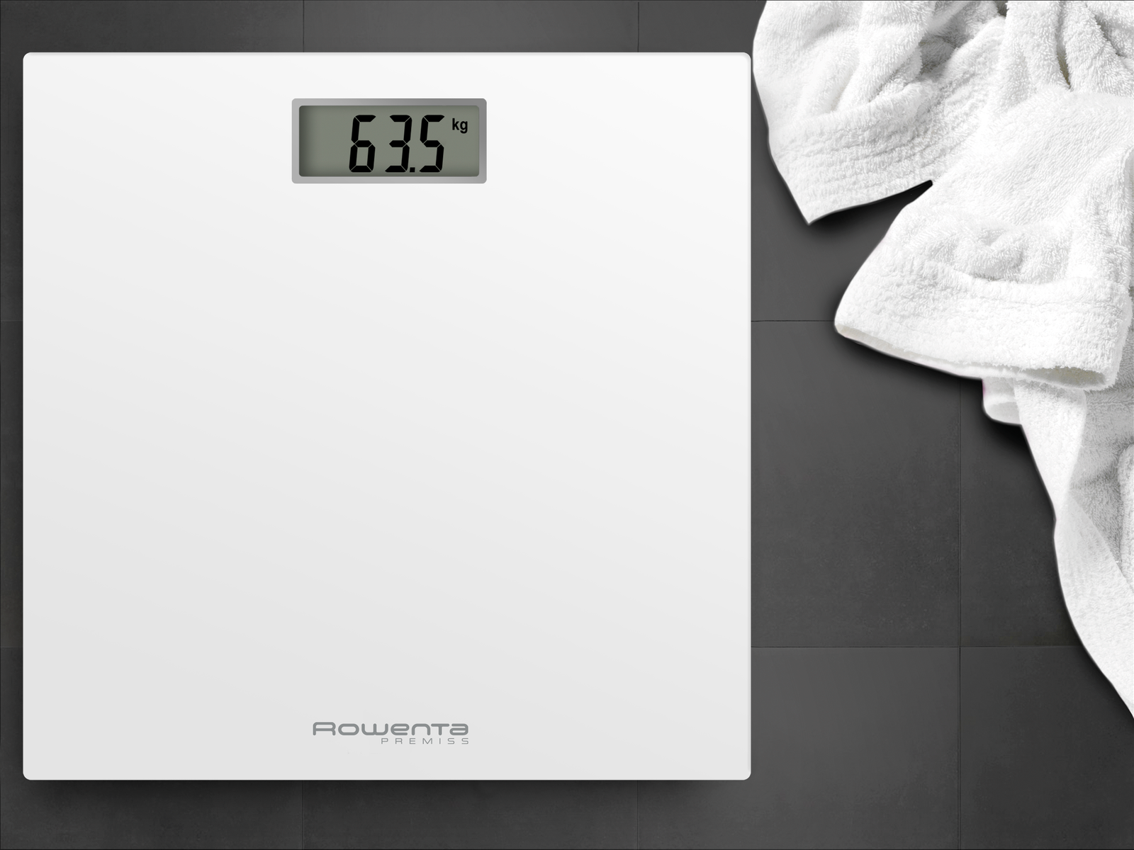 Una báscula digital de baño blanca con 63.5 kg, junto a una toalla blanca.