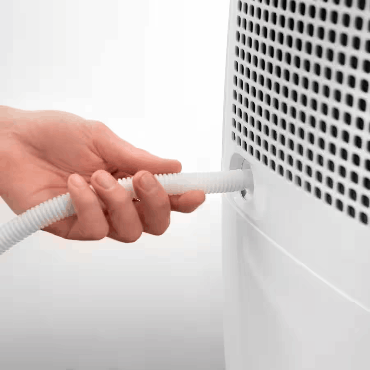 Ręka wkłada białą karbowaną rurkę do białego urządzenia z czarną kratką.