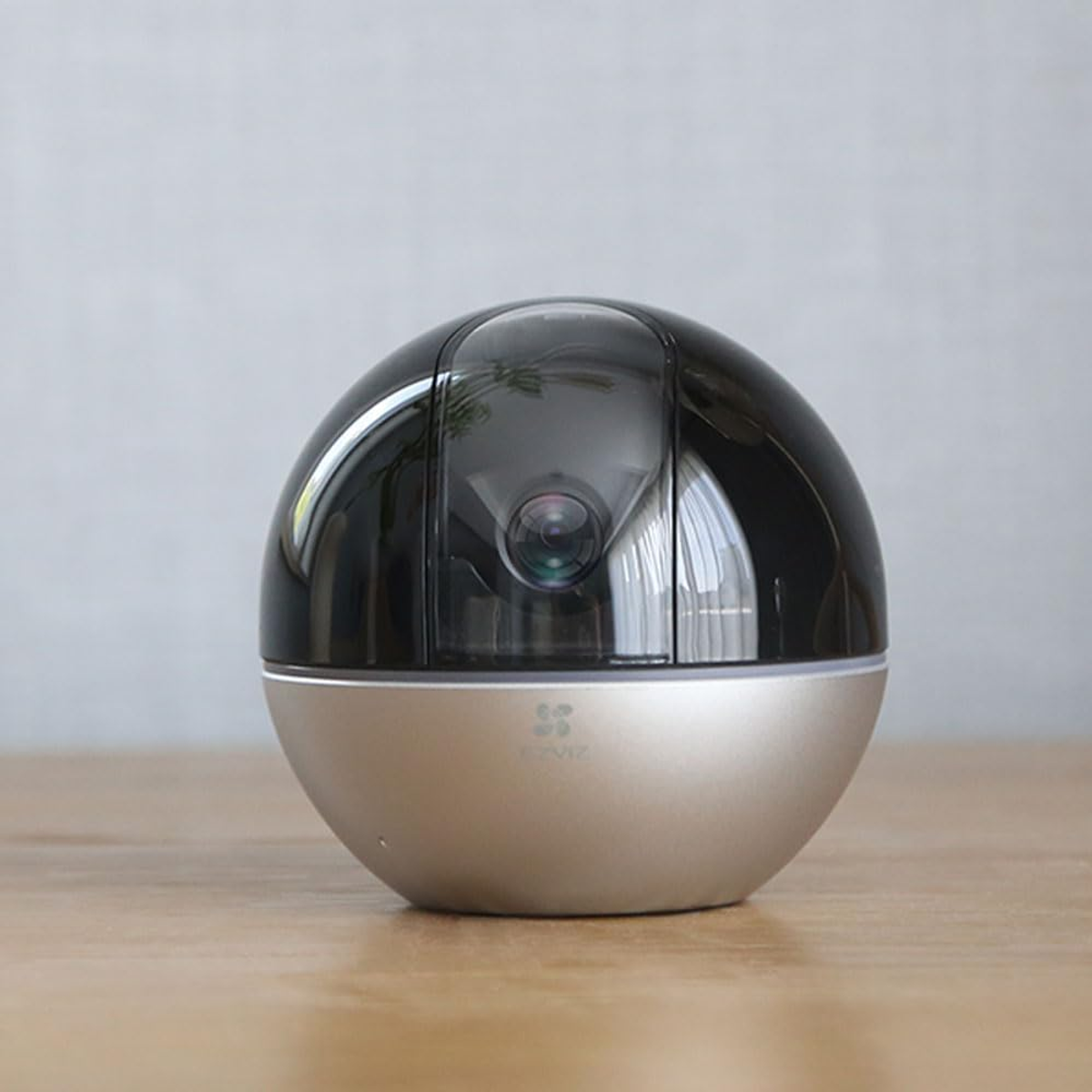 Czarno-złota kamera bezpieczeństwa, sferyczna, na drewnianej powierzchni, z szarym tłem.