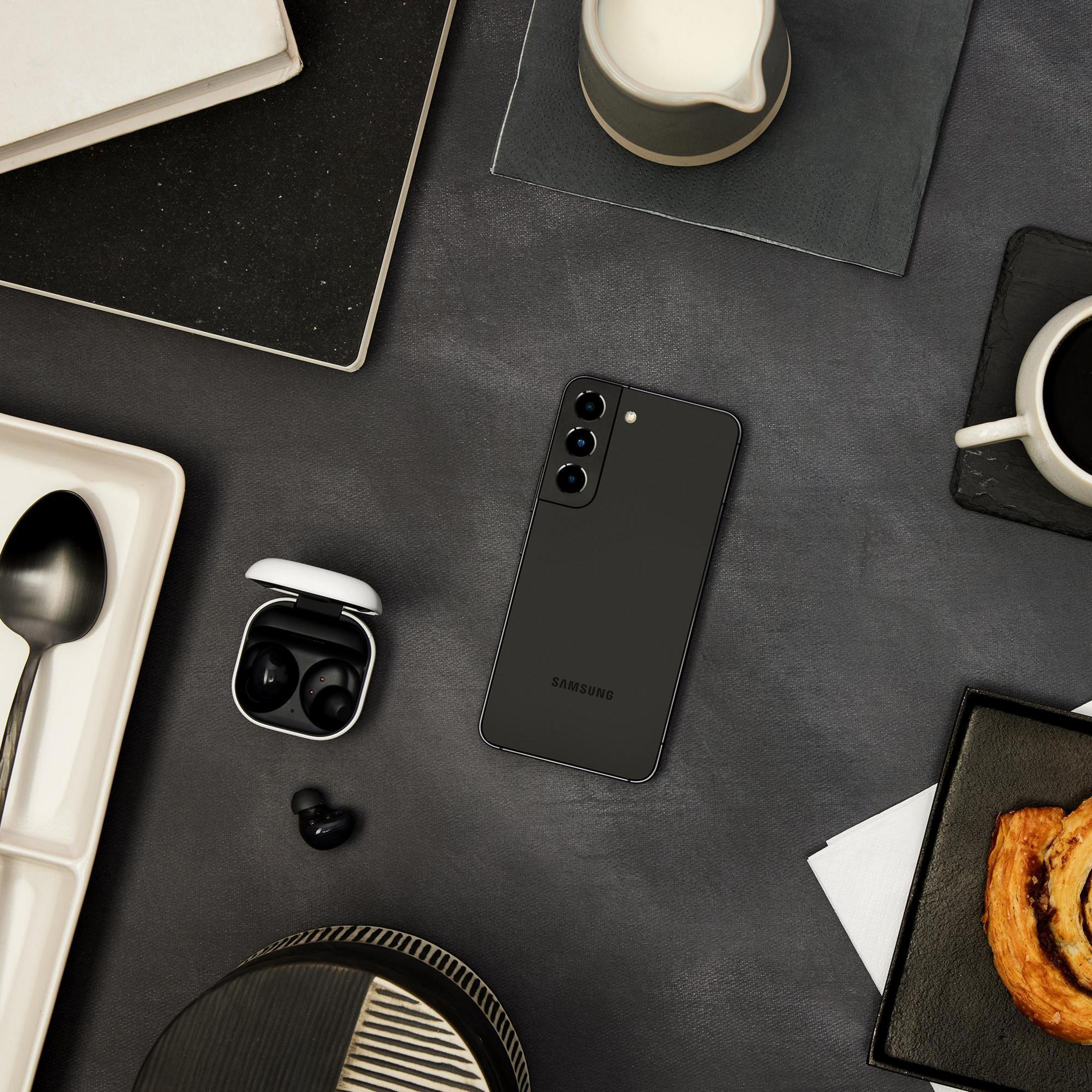 Widok z góry z smartfonem, słuchawkami, kawą i ciastkiem na stole.