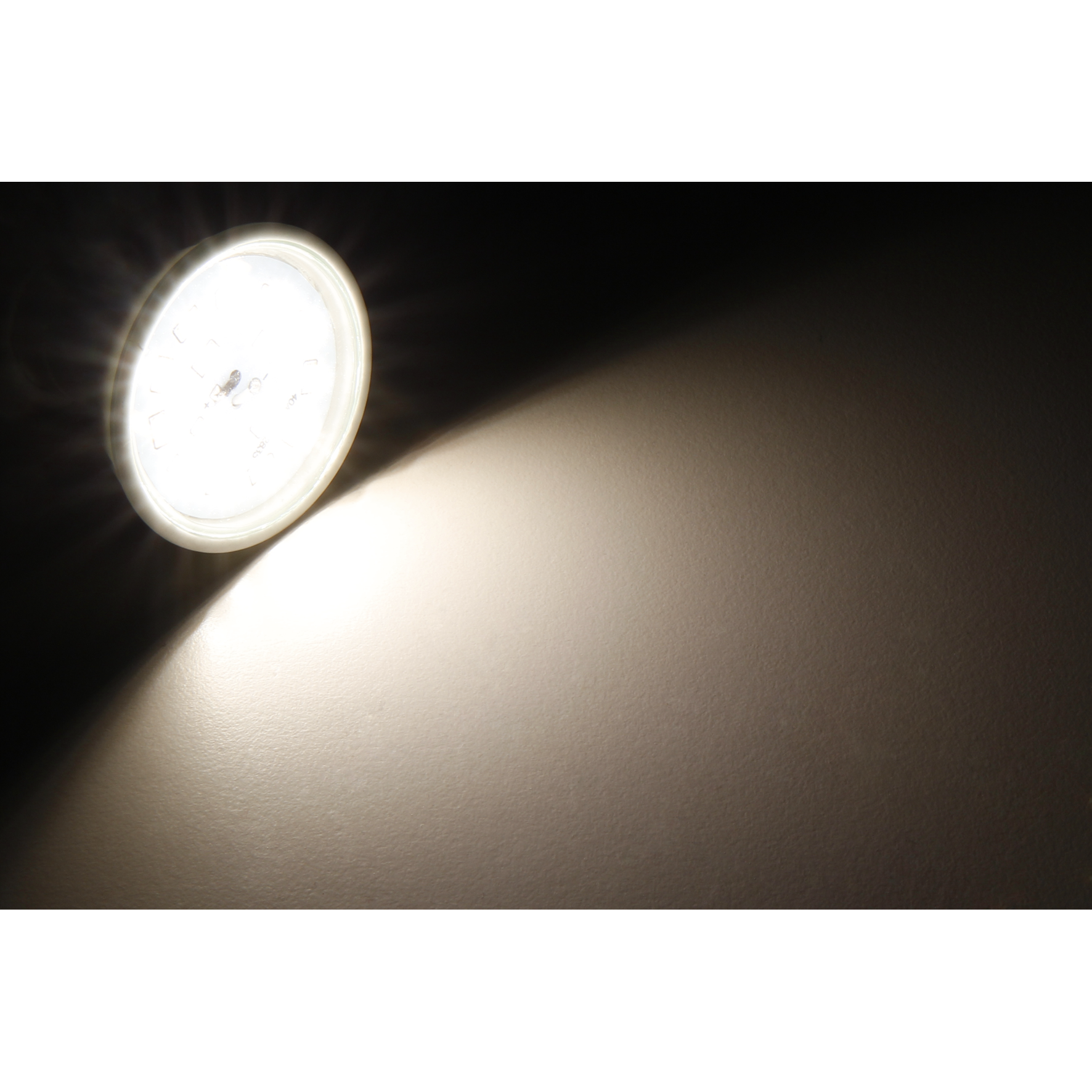 Ein heller Scheinwerfer, der auf eine Wand scheint. Die Lichtquelle ist eine kreisförmige Lampe, der Strahl konisch.