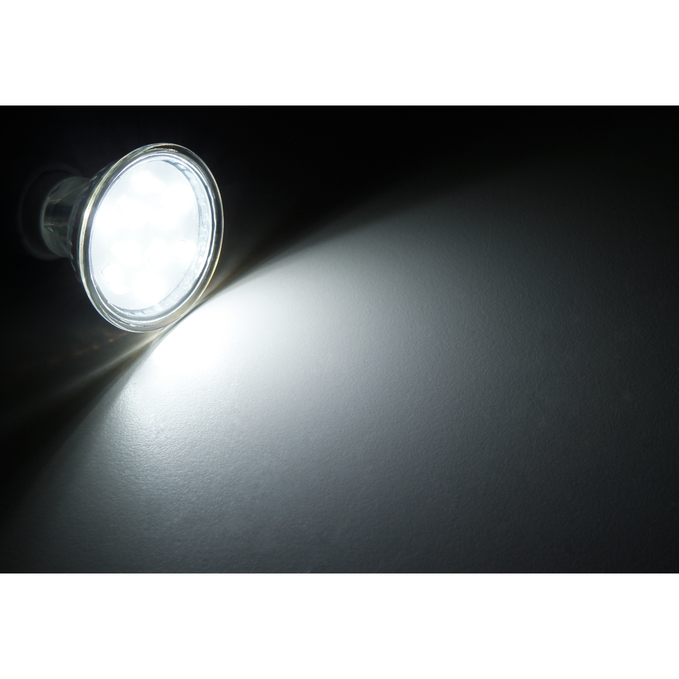Ein helles Licht, das von einer Lampe in einem dunklen Raum scheint. Das Licht reflektiert an der Wand.