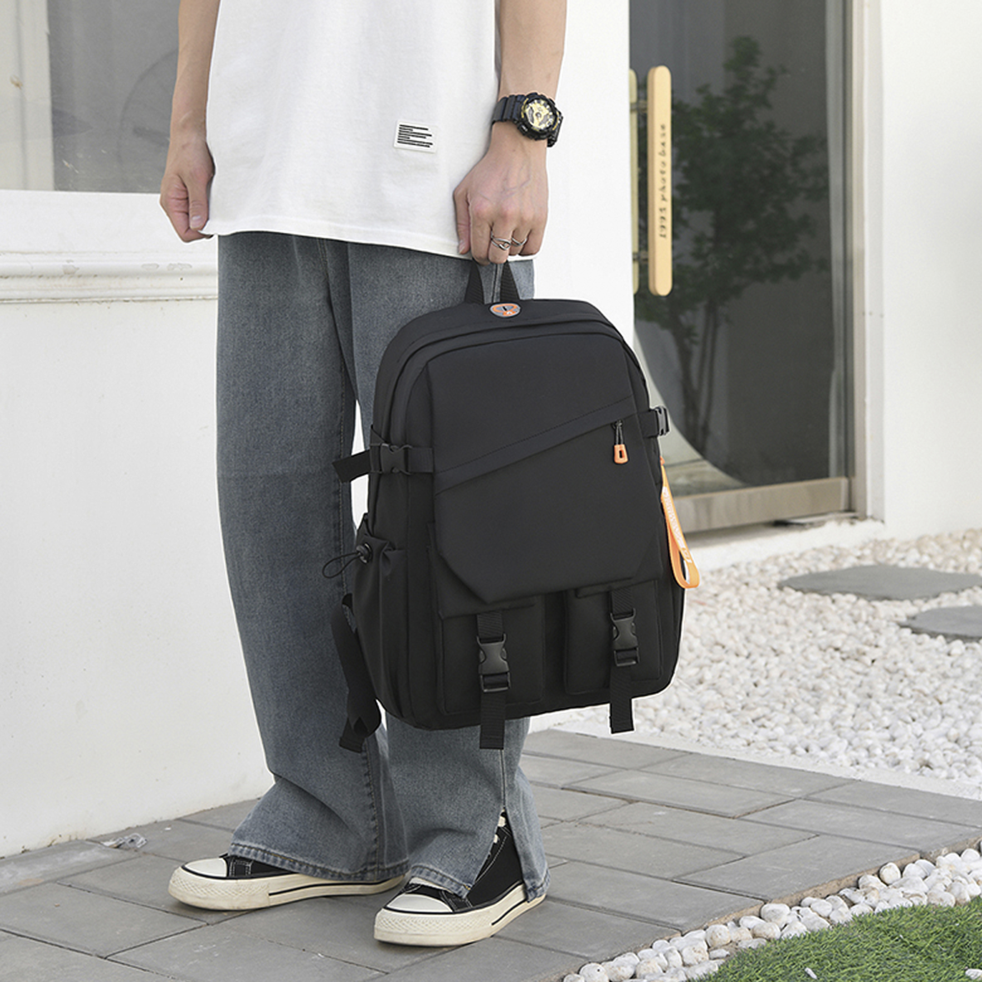 Un uomo con uno zaino è in piedi fuori. Indossa jeans e scarpe da ginnastica. La borsa è nera.