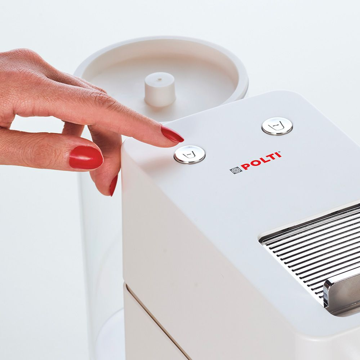 El dedo de una mujer presiona un botón en un electrodoméstico Polti blanco. Esmalte de uñas rojo visible.