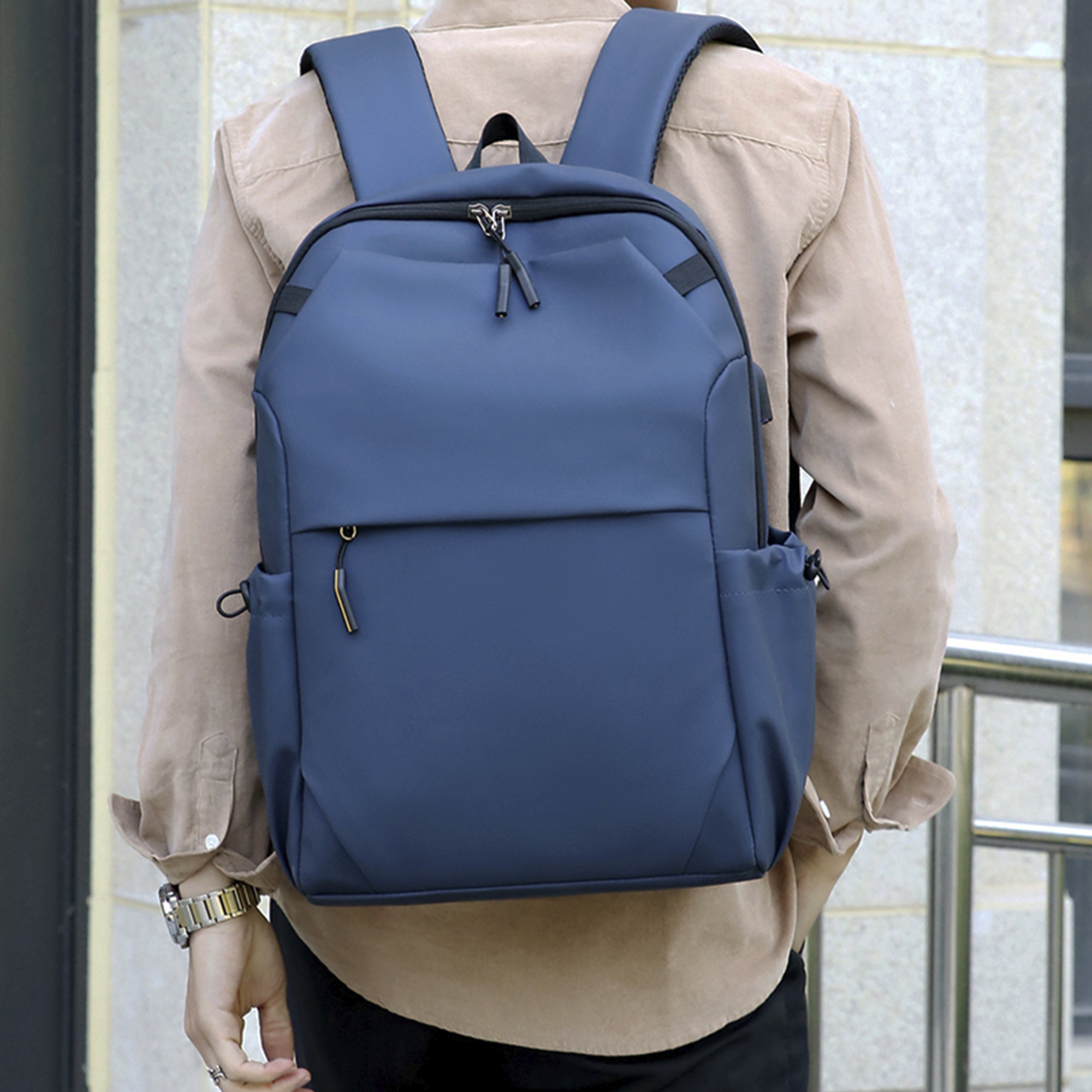 Una persona con una camicia marrone indossa uno zaino blu con tasche multiple e una cerniera.