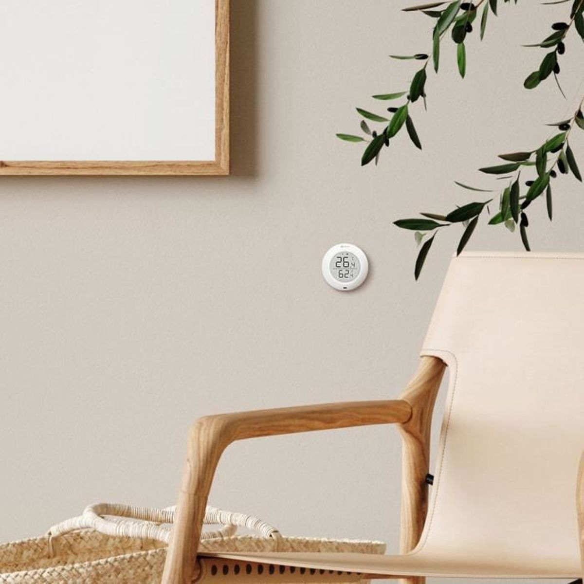 Biały czujnik z wyświetlaczem pokazującym liczby. Krzesło, roślina i ramka na zdjęcia są w tle.