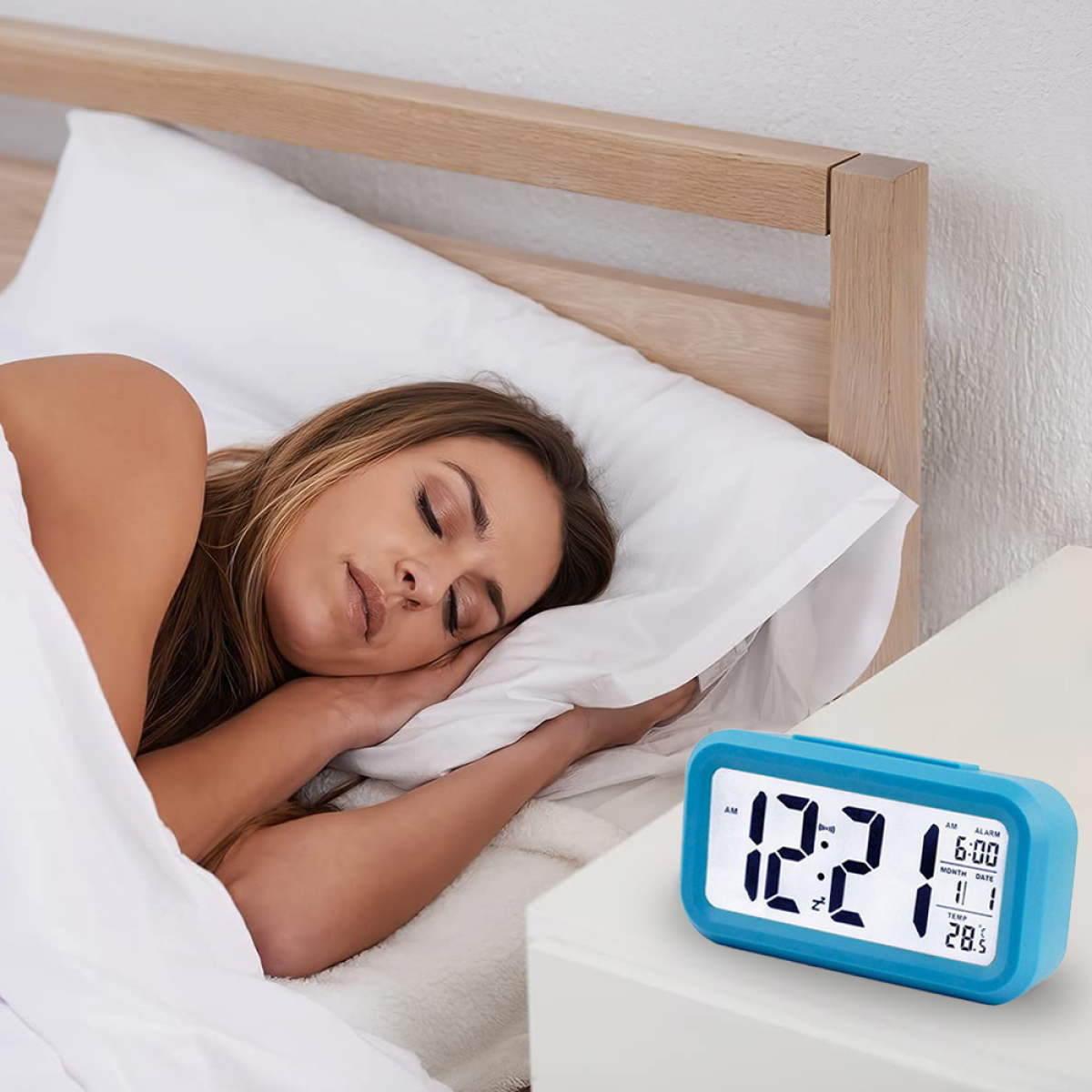 Eine Frau schläft im Bett, mit einem blauen digitalen Wecker auf dem Nachttisch, der Zeit und Datum anzeigt.