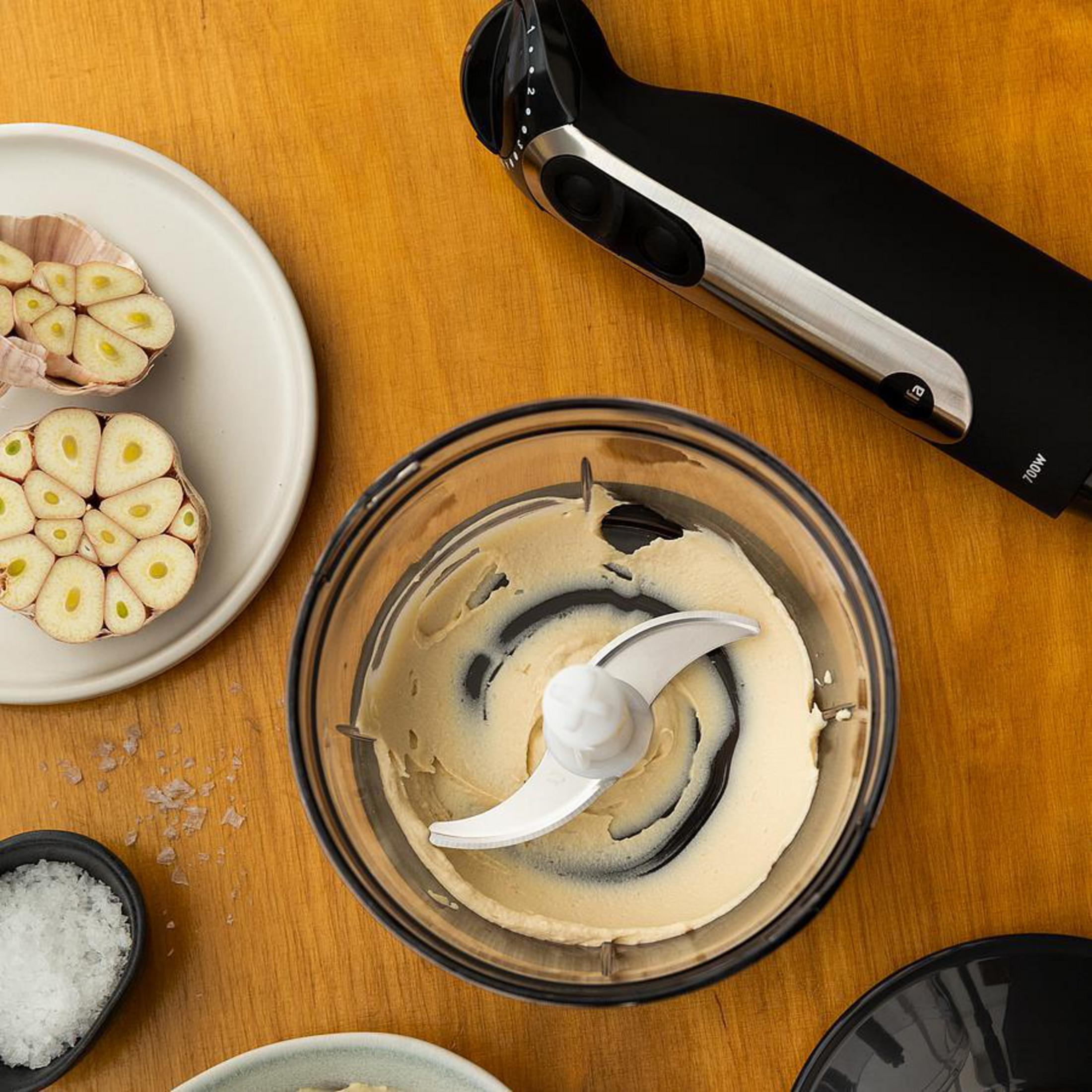 Un procesador de alimentos con una cuchilla dentro y dientes de ajo cortados a un lado.