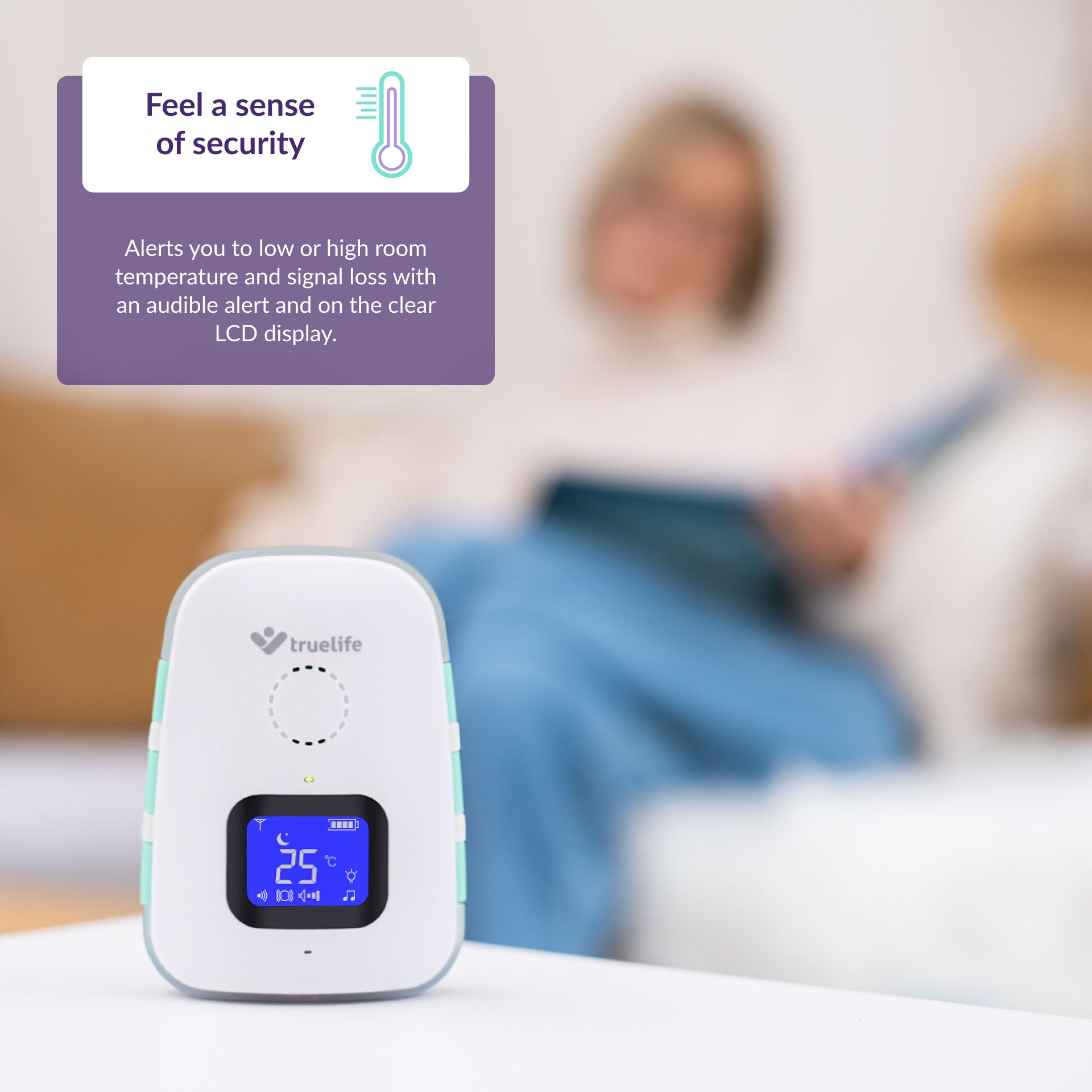 Biały niania elektroniczna z niebieskim ekranem na stole, osoba w tle jest niewyraźna.