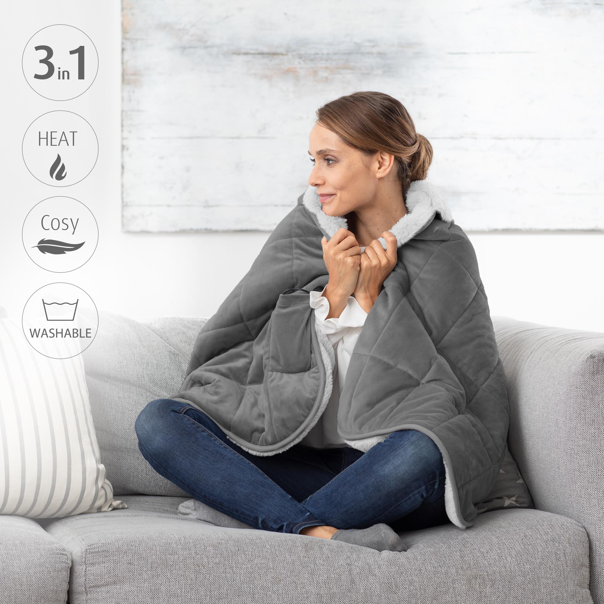 Una donna avvolta in una coperta grigia trapuntata siede su un divano. Le icone indicano calore, accogliente e lavabile.
